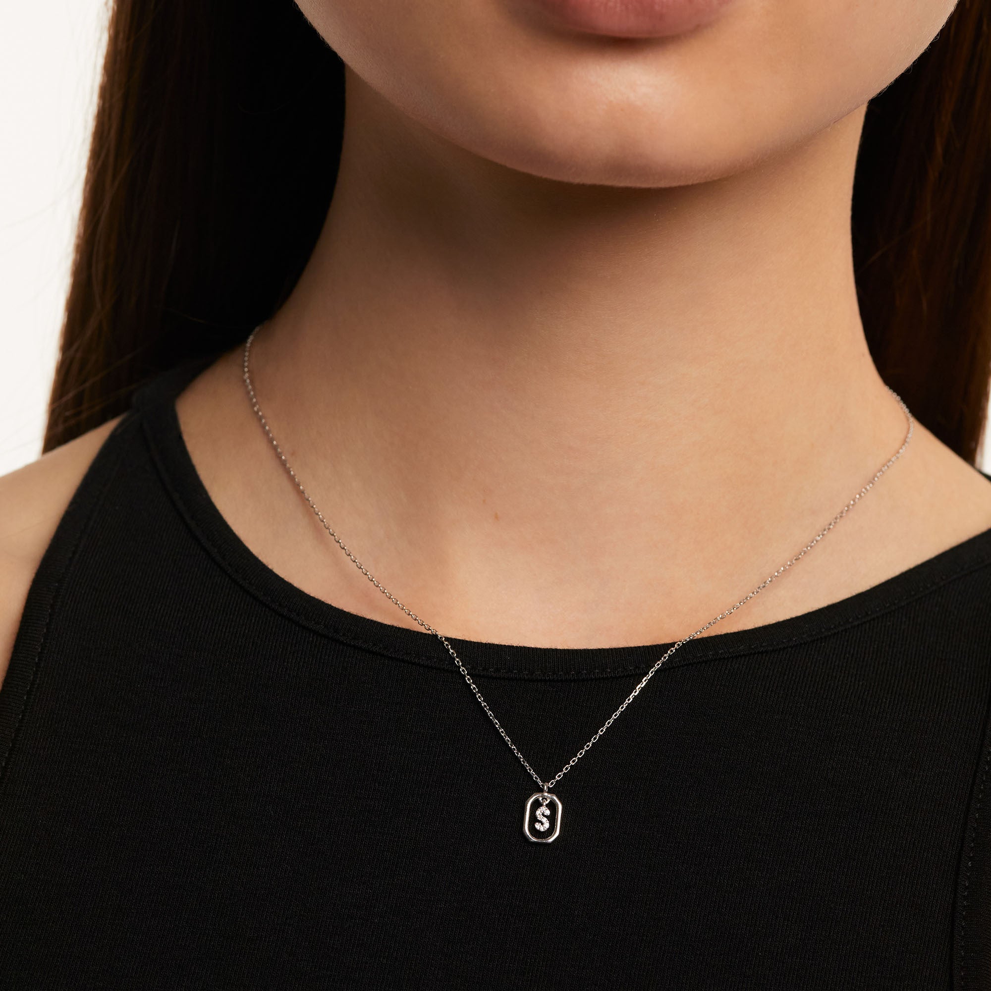 Eine Frau in einem schwarzen ärmellosen Oberteil trägt die PDPaola Halskette - The Mini Letter S von PDPaola, die aus 925er Sterlingsilber gefertigt und mit funkelnden Zirkonia verziert ist.