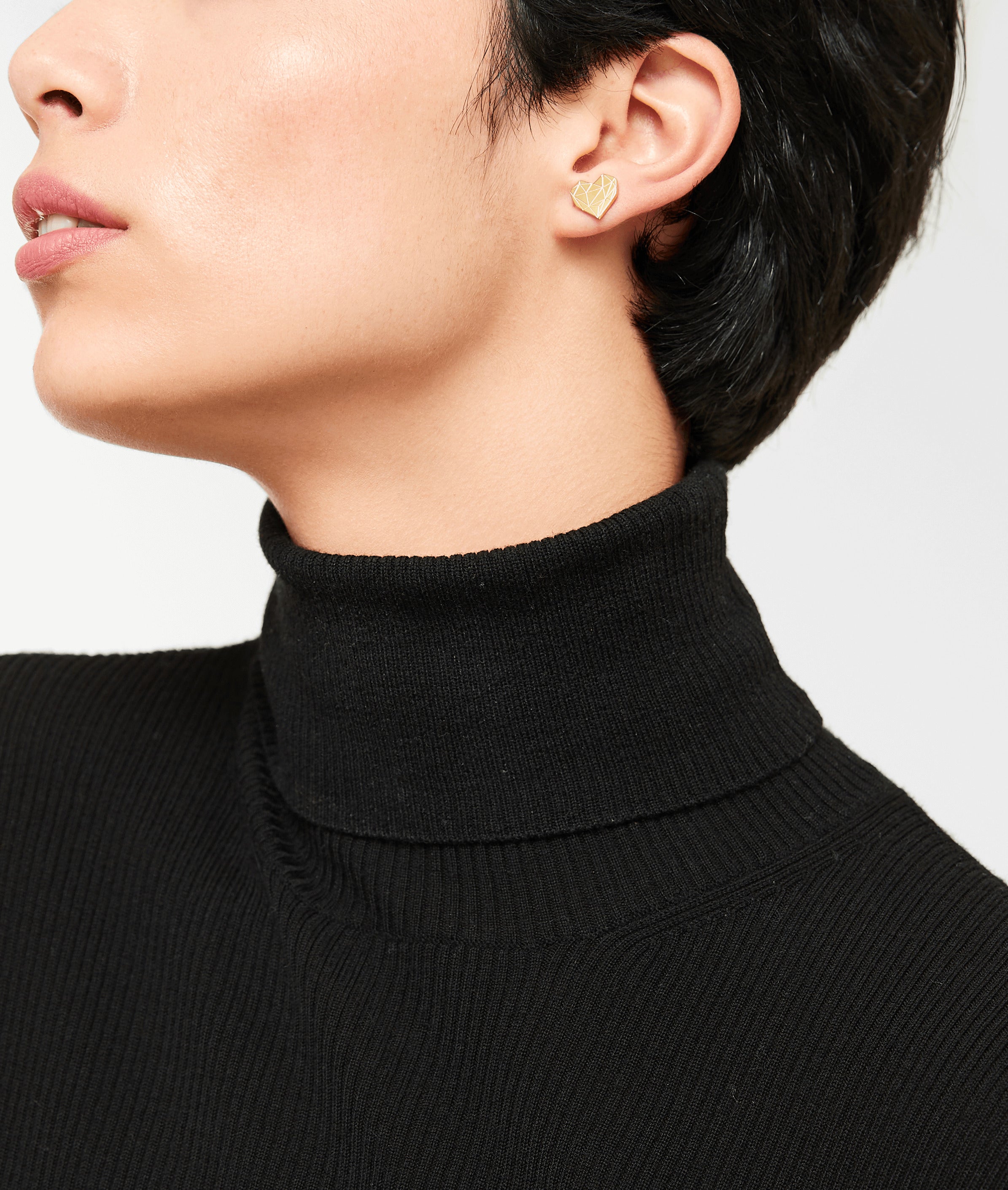 Person trägt einen schwarzen Rollkragenpullover und goldene Ohrstecker in Herzform, gepaart mit dem LIEBESKIND BERLIN Set - Broken Heart von Liebeskind Berlin, von den Schultern aufwärts gezeigt.
