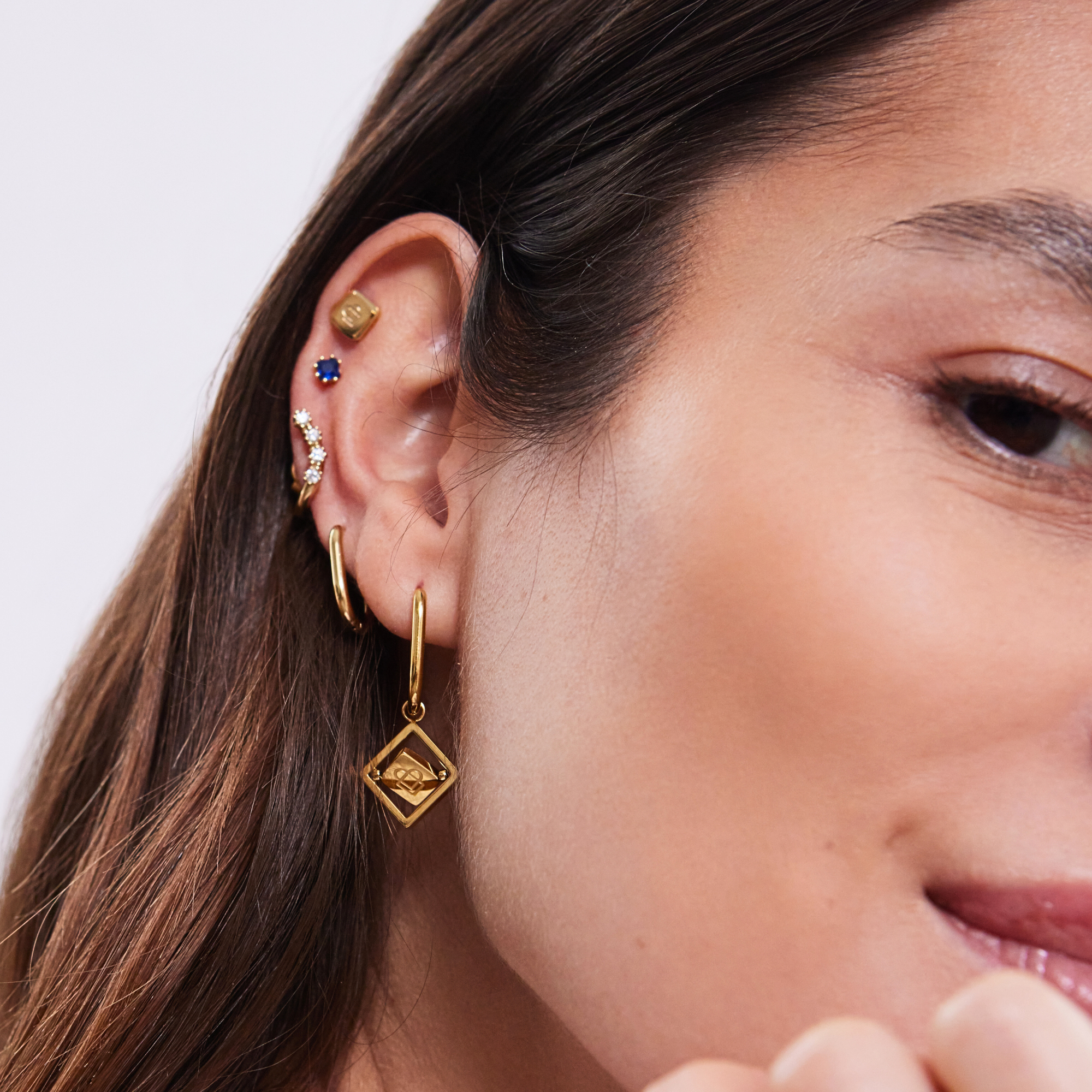 Nahaufnahme eines weiblichen Ohrs mit mehreren goldenen Ohrringen und funkelnden Piercings.