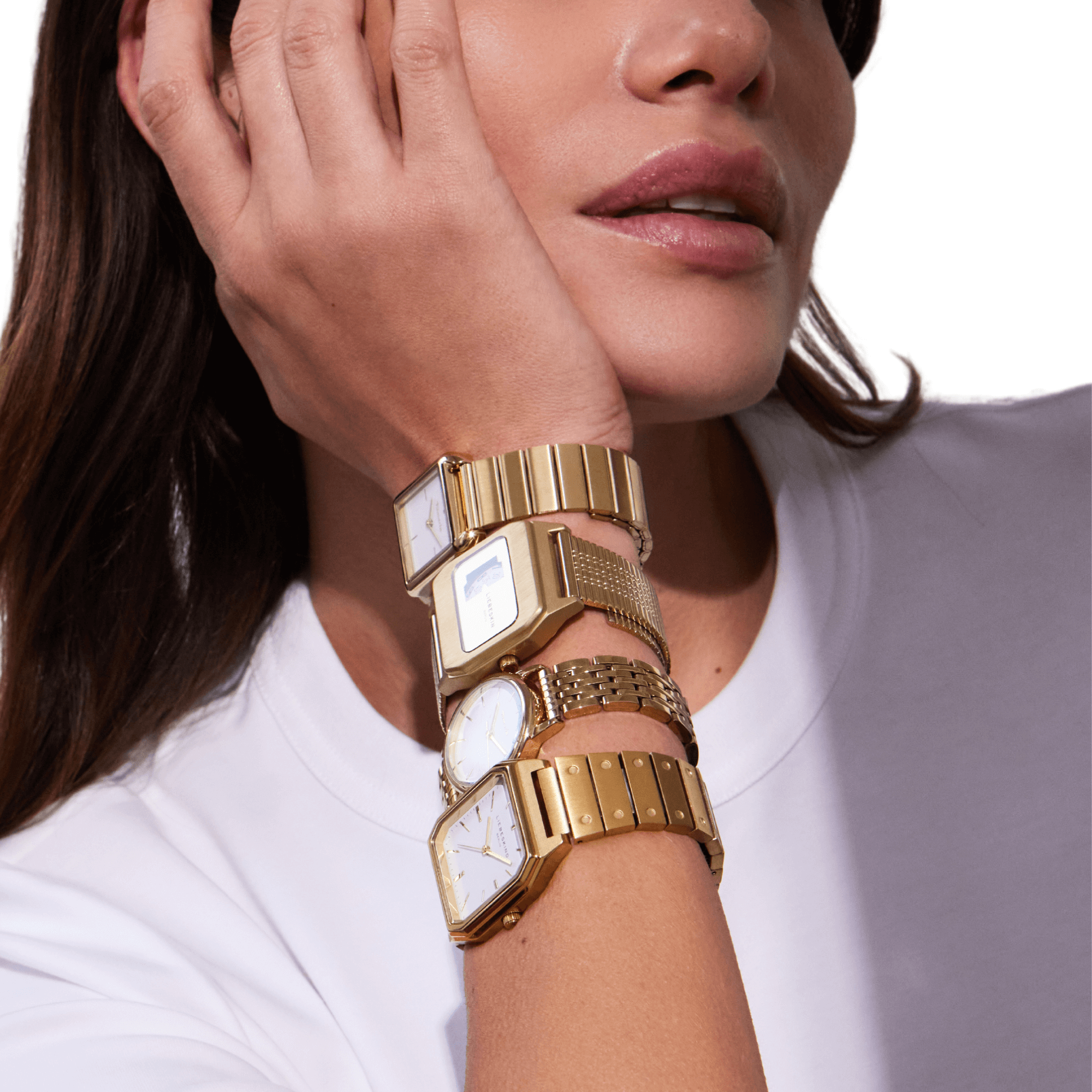Frau mit weißem T-Shirt trägt fünf goldene Armbanduhren am linken Handgelenk, Kopf aufgestützt.