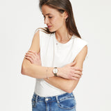 Frau in weißem ärmellosen Oberteil und blauer Jeans, Arme verschränkt, hebt dezentes Ear Candy mit elegantem Tamaris Ohrstecker - Baguette von Tamaris vor einem schlichten Hintergrund hervor.