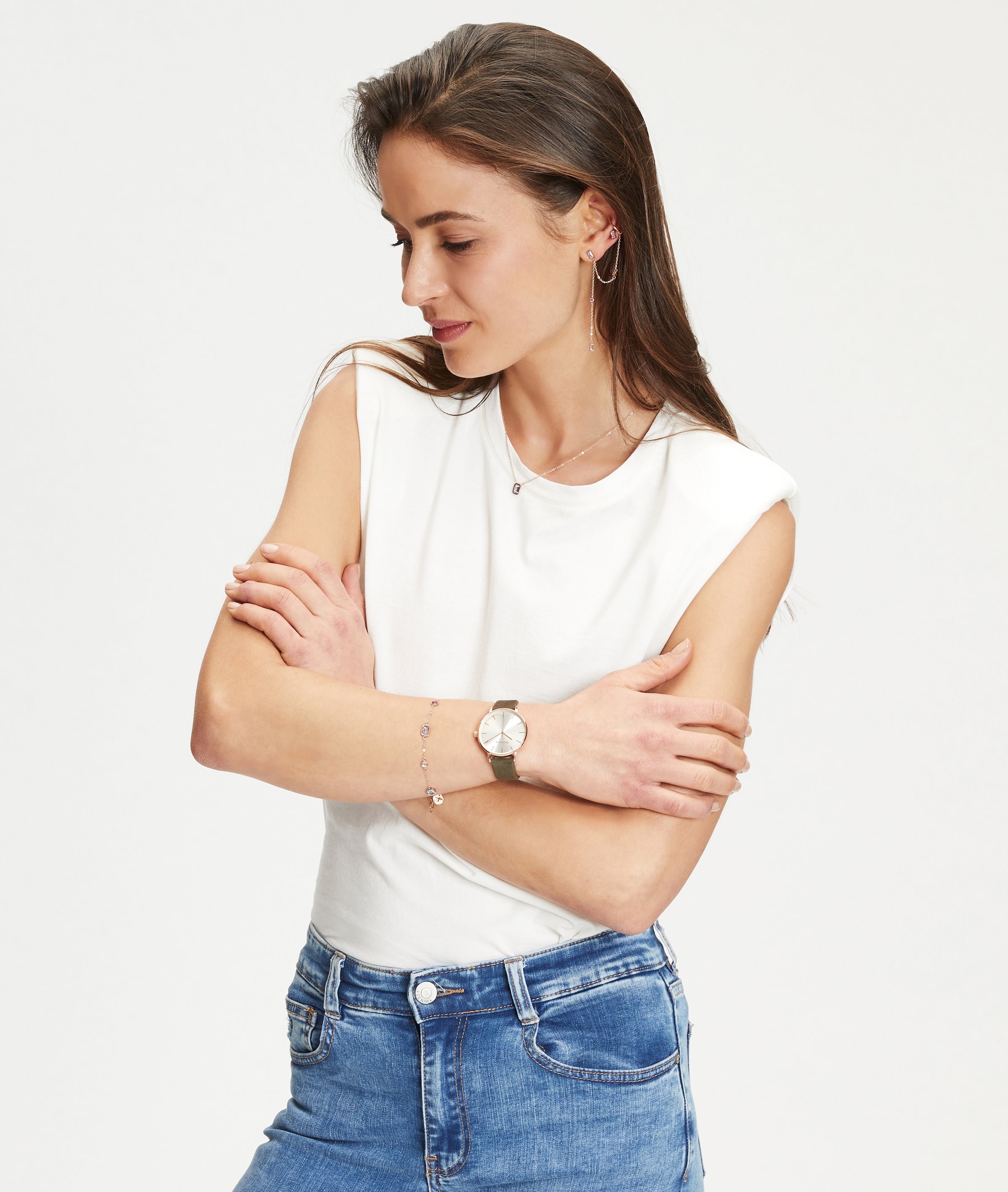 Frau in weißem ärmellosen Oberteil und blauer Jeans, Arme verschränkt, hebt dezentes Ear Candy mit elegantem Tamaris Ohrstecker - Baguette von Tamaris vor einem schlichten Hintergrund hervor.