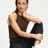 Eine Frau in einem braunen ärmellosen Oberteil und schwarzen Jeans sitzt mit einem Knie hoch, trägt weiße Turnschuhe und Tamaris Ohrstecker - Baguette by Tamaris, die ihrem Look einen eleganten Touch von Ohrschmuck verleihen.
