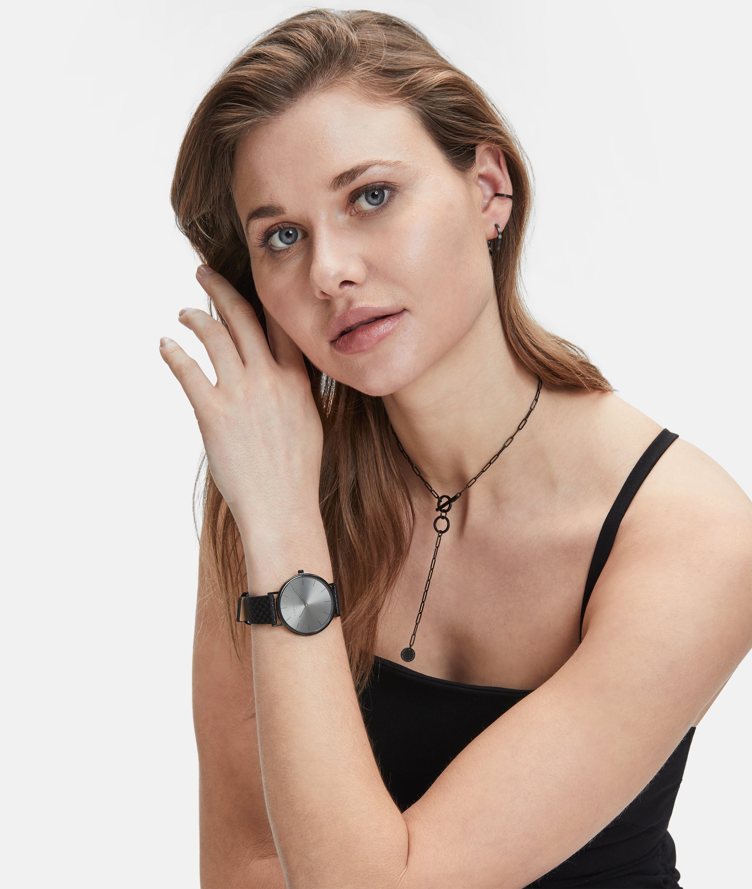 Frau mit hellbraunem Haar trägt ein schwarzes Tanktop, Uhr, Halskette und die LIEBESKIND BERLIN Ear Cuff - The Small Basic Logo by Liebeskind Berlin, wobei sie ihr Ohr berührt und nach vorne schaut.