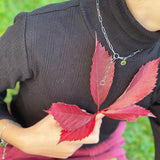 Eine Person in einem schwarzen Rollkragenpullover hält rote Herbstblätter und zeigt die Cool Time Kids Halskette - The Cool Mini Link von Cool Time mit einer eleganten silbernen Halskette und einem Armband.