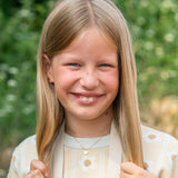 Junges Mädchen mit langen blonden Haaren lächelt im Freien, trägt ein beiges Top mit weißen Blumen und präsentiert die Cool Time Kids Halskette - The Cool Smiley von Cool Time.