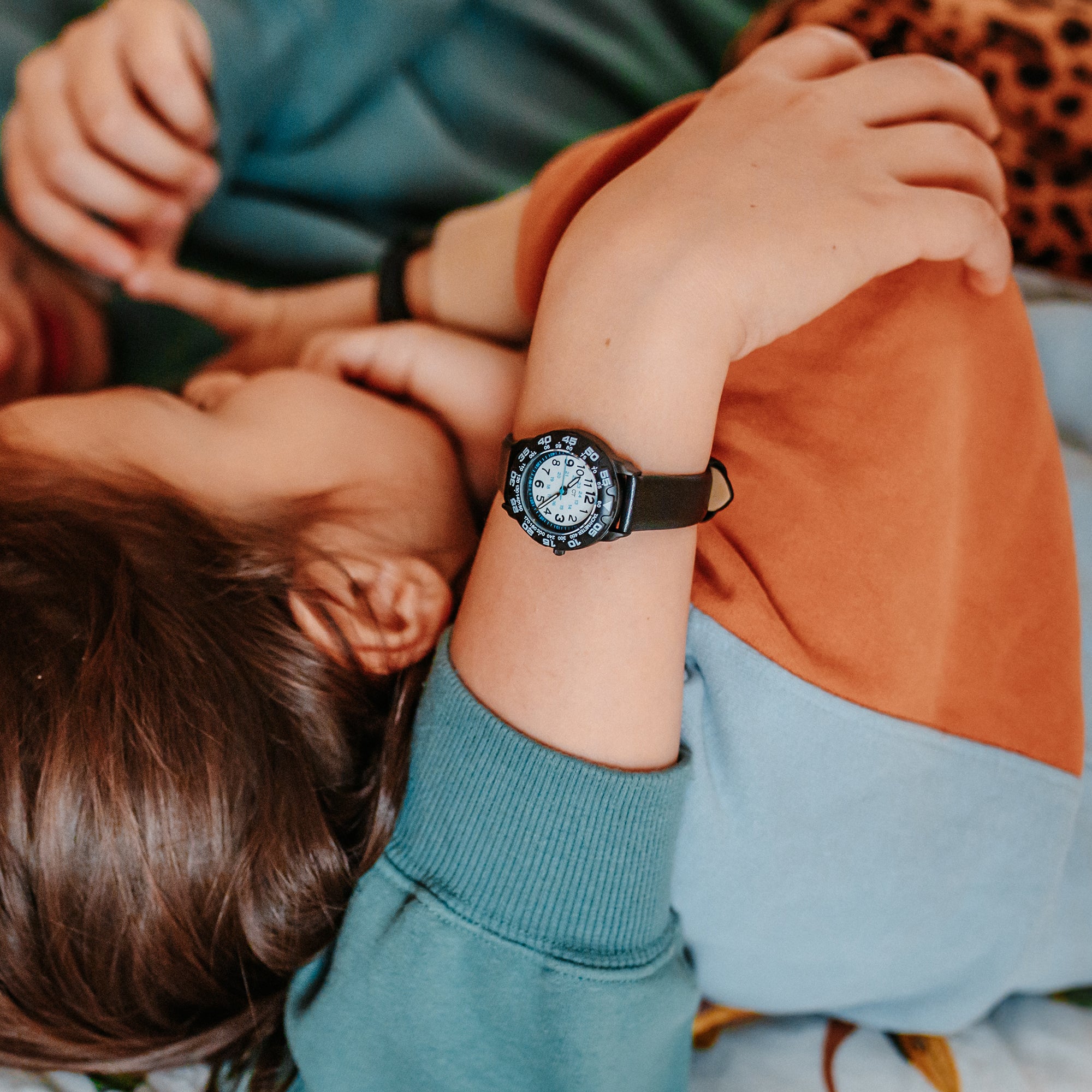 Ein Kind, das die Cool Time Kids Armbanduhr - The Cool Classic Black von Cool Time trägt, liegt in bunter Kleidung mit erhobenem Arm - das perfekte Geschenk für junge Uhrenliebhaber.