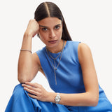 Frau in blauem ärmellosen Oberteil und Hose, die Liebeskind Berlin Schmuck im Lagenlook und die LIEBESKIND BERLIN Halskette - The Nugget trägt, schaut ernst in die Kamera.