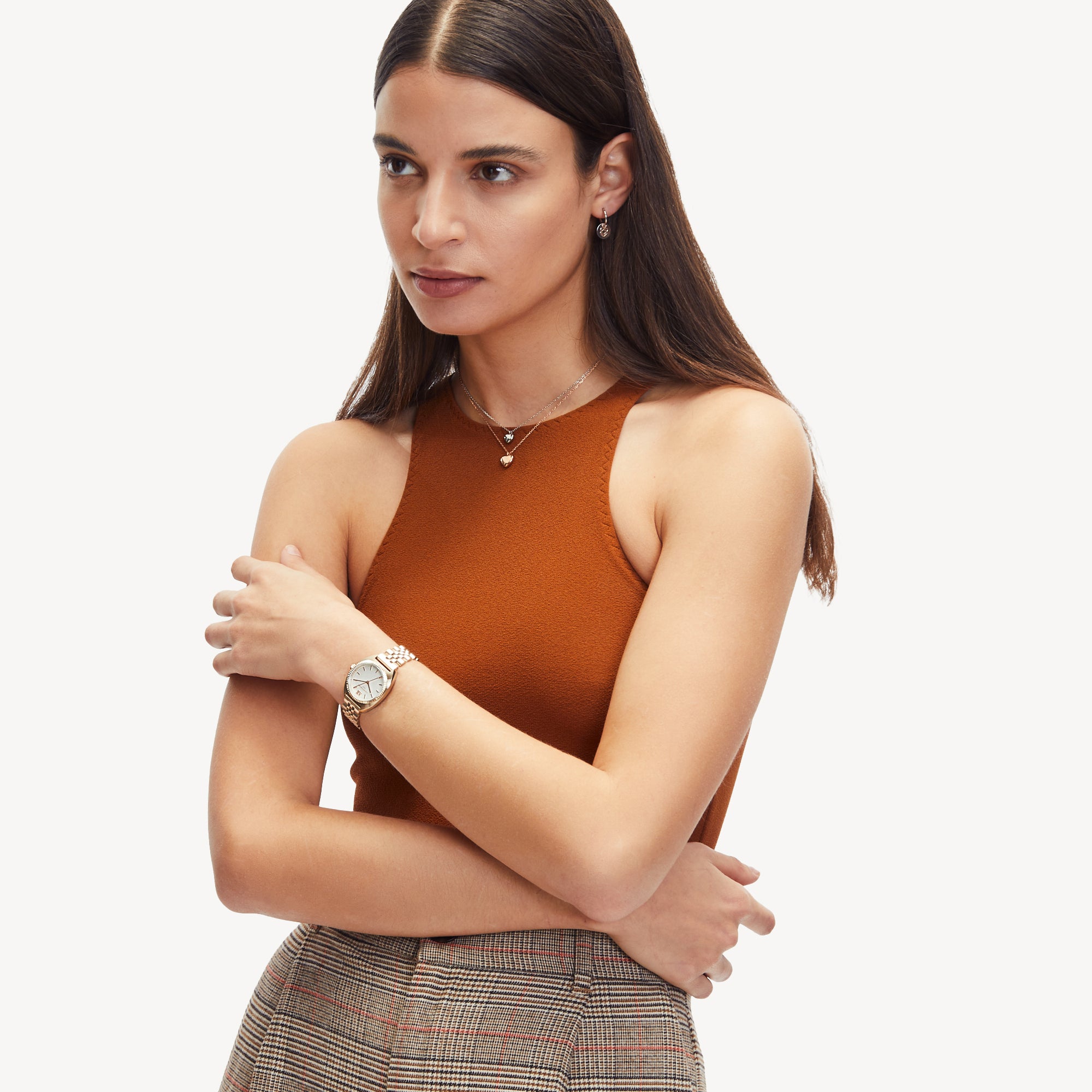 Frau in einem orangefarbenen ärmellosen Oberteil und einer karierten Hose. Sie trägt die Liebeskind Berlin Creole - Keep Loving Ohrringe, eine Uhr und Schmuck und hat die Arme verschränkt.