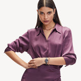 Eine Frau in einem lilafarbenen Seidenkleid posiert selbstbewusst mit der Liebeskind Berlin Halskette - The Knot und einer Uhr und setzt damit einen extravaganten Look vor einem schlichten Hintergrund in Szene.