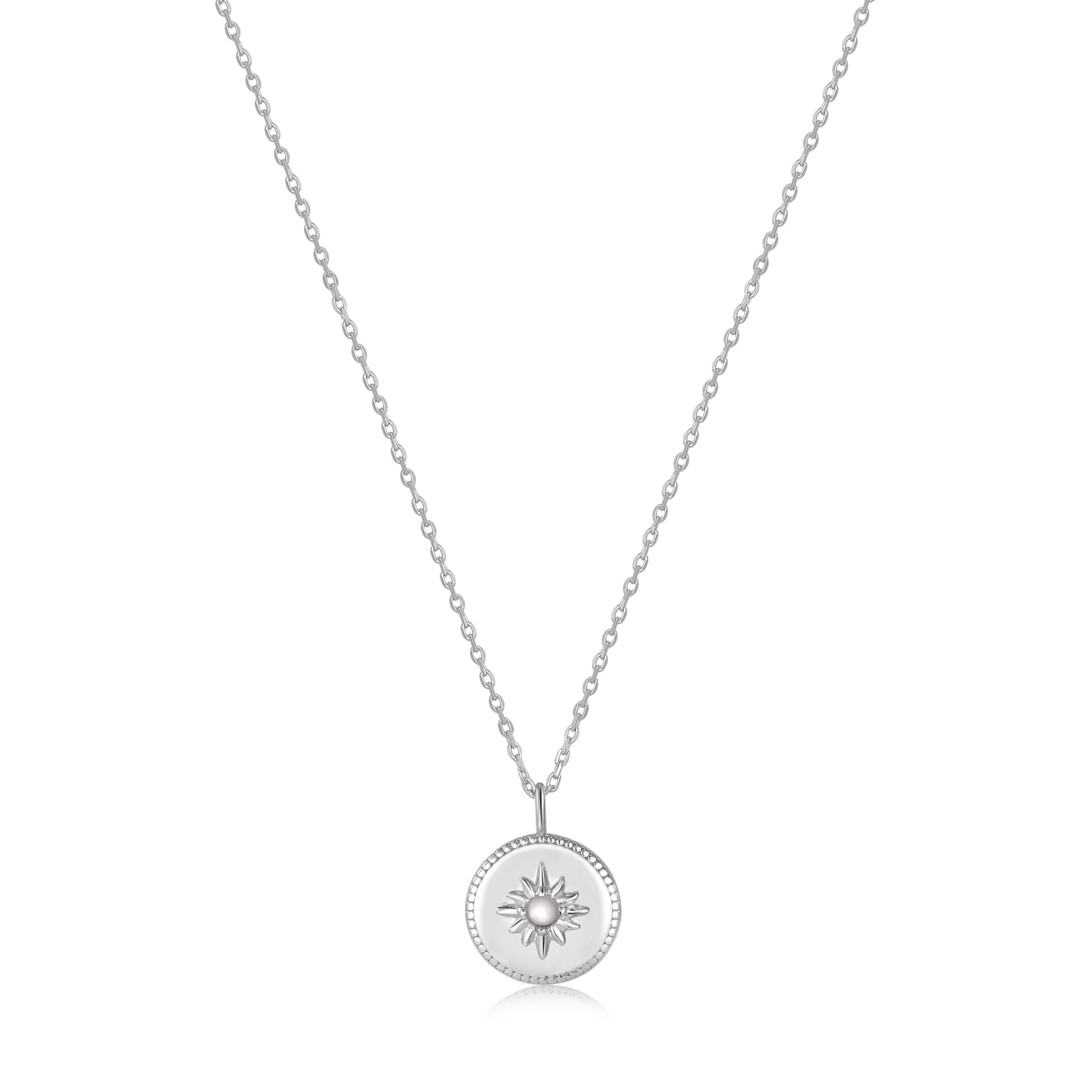 Die Ania Haie Halskette - The Star Coin Pendant besteht aus einer silbernen Kette und einem runden Sunburst-Anhänger mit einem zentralen Edelstein. Erleben Sie die Eleganz von Ania Haie mit dieser außergewöhnlichen Halskette.