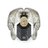 Eine Philipp Plein Armbanduhr - The Golden $keleton wird in einer geometrischen, totenkopfförmigen Glasvitrine auf einem schwarzen, marmorierten Sockel präsentiert.