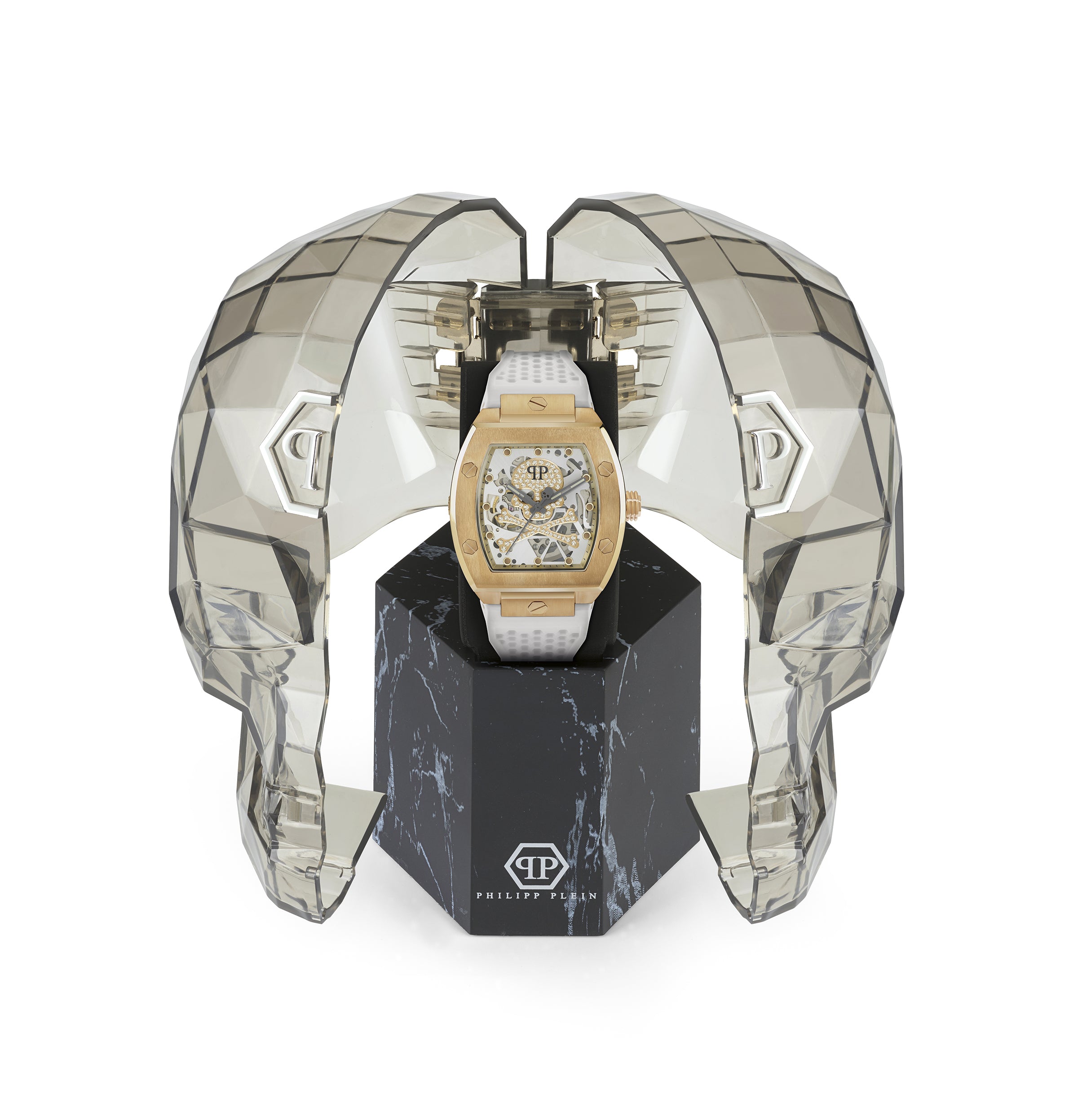 Die Philipp Plein Armbanduhr - The White Golden $keleton von Philipp Plein präsentiert sich in einem transparenten, geometrischen Gehäuse in Form eines Totenkopfes auf einem schwarzen Ständer.