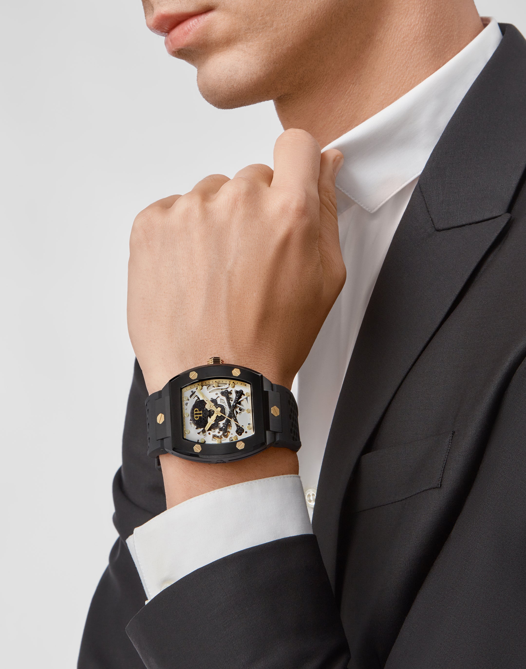 Ein Mann in schwarzem Anzug und weißem Hemd trägt eine Philipp Plein Armbanduhr - The Black $keleton von Philipp Plein an seinem linken Handgelenk.