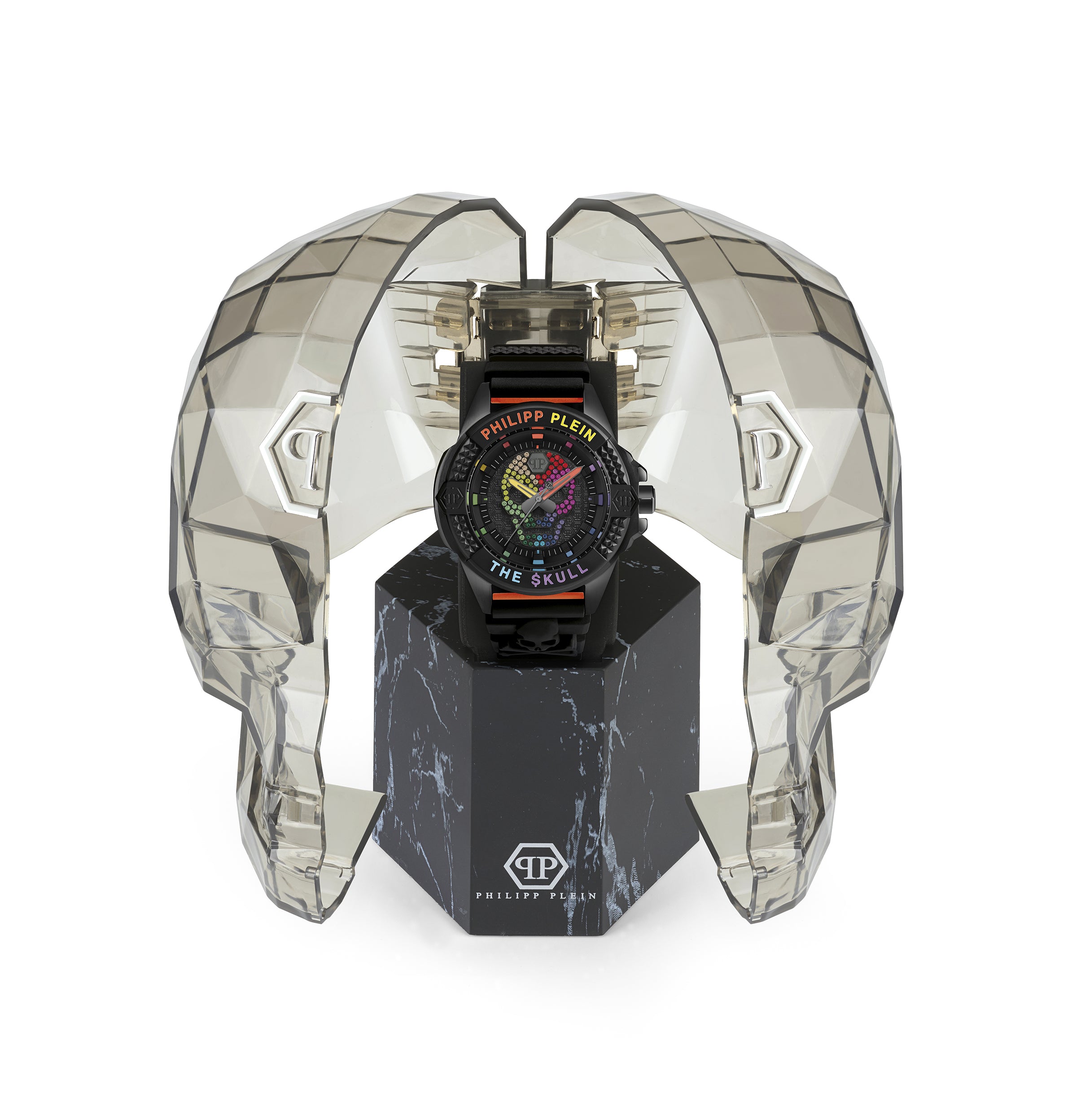 Die Philipp Plein Armbanduhr - The Bold Color $kull präsentiert sich mit Regenbogendetails in einem geometrischen, durchscheinenden, totenkopfförmigen Gehäuse auf einem schwarzen Ständer und spiegelt den kühnen Geist von Philipp Plein wider.