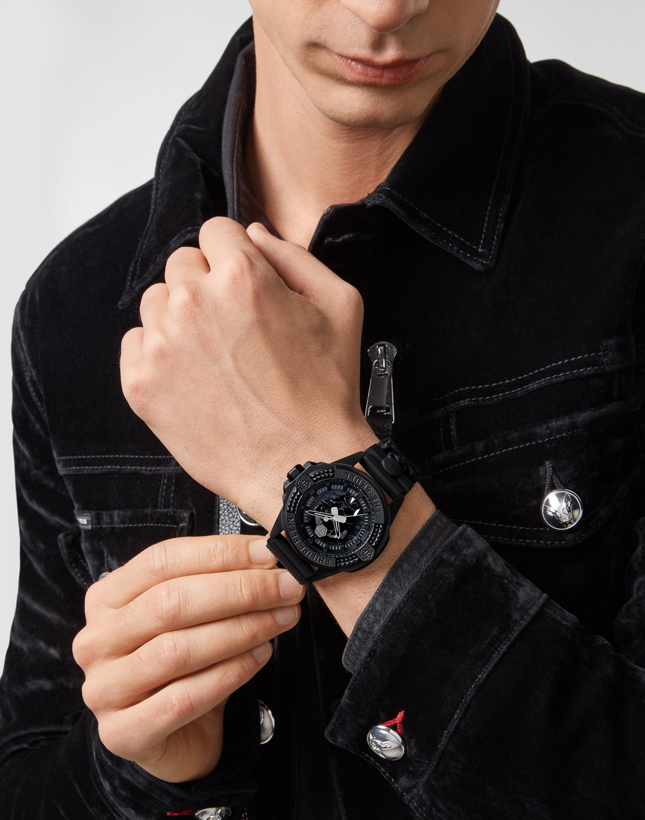 Ein Mann in einer schwarzen Jacke legt eine Philipp Plein Armbanduhr - The Solid Black $kull von Philipp Plein an seinem linken Handgelenk an.
