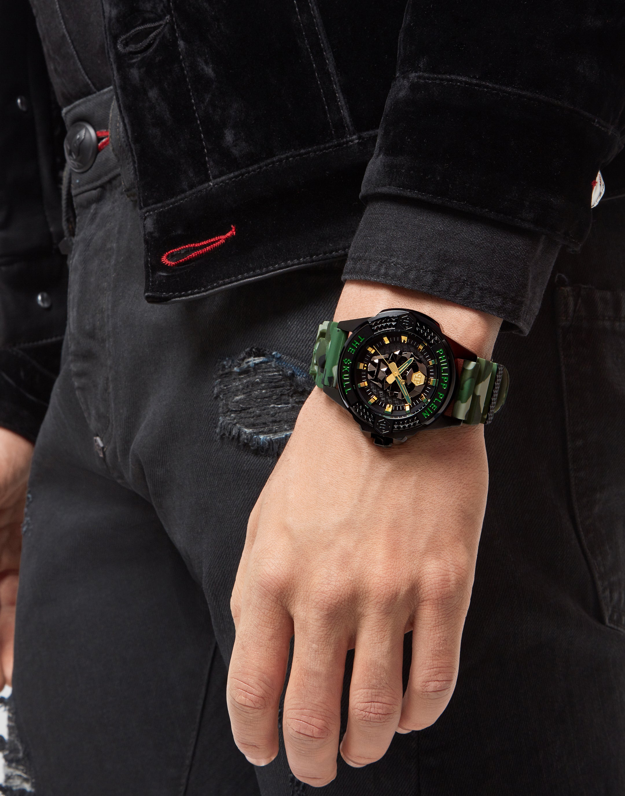 Eine Person trägt eine Philipp Plein Armbanduhr - The Camouflage $kull von Philipp Plein und ein schwarzes Denim-Outfit mit zerrissenen Jeans.