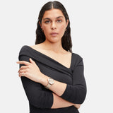 Frau mit schwarzem schulterfreiem Oberteil, die ihre Arme verschränkt und die Creole - The Riffle von Liebeskind Berlin trägt, vor einem schlichten Hintergrund.