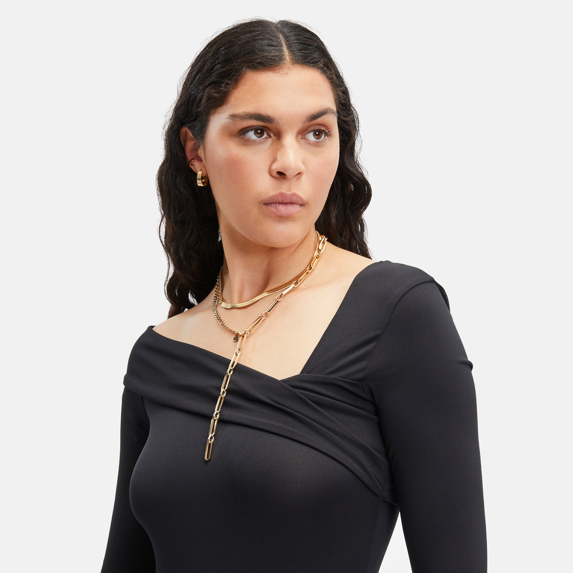 Frau mit schwarzem schulterfreiem Oberteil trägt mehrere goldene Liebeskind Berlin-Halsketten und die LIEBESKIND BERLIN Creole - The Riffle, mit Blick zur Seite.