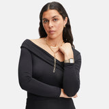 Eine Frau mit einem schwarzen schulterfreien Top, mehreren goldenen Halsketten, einer Edelstahl-Uhr und der LIEBESKIND BERLIN Creole - The Riffle von Liebeskind Berlin posiert mit verschränkten Armen.