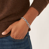 Eine Person, die ein Fossil Heritage D-Link Armband, einen braunen Pullover und eine blaue Jeans trägt und die Hand in der Tasche hat.