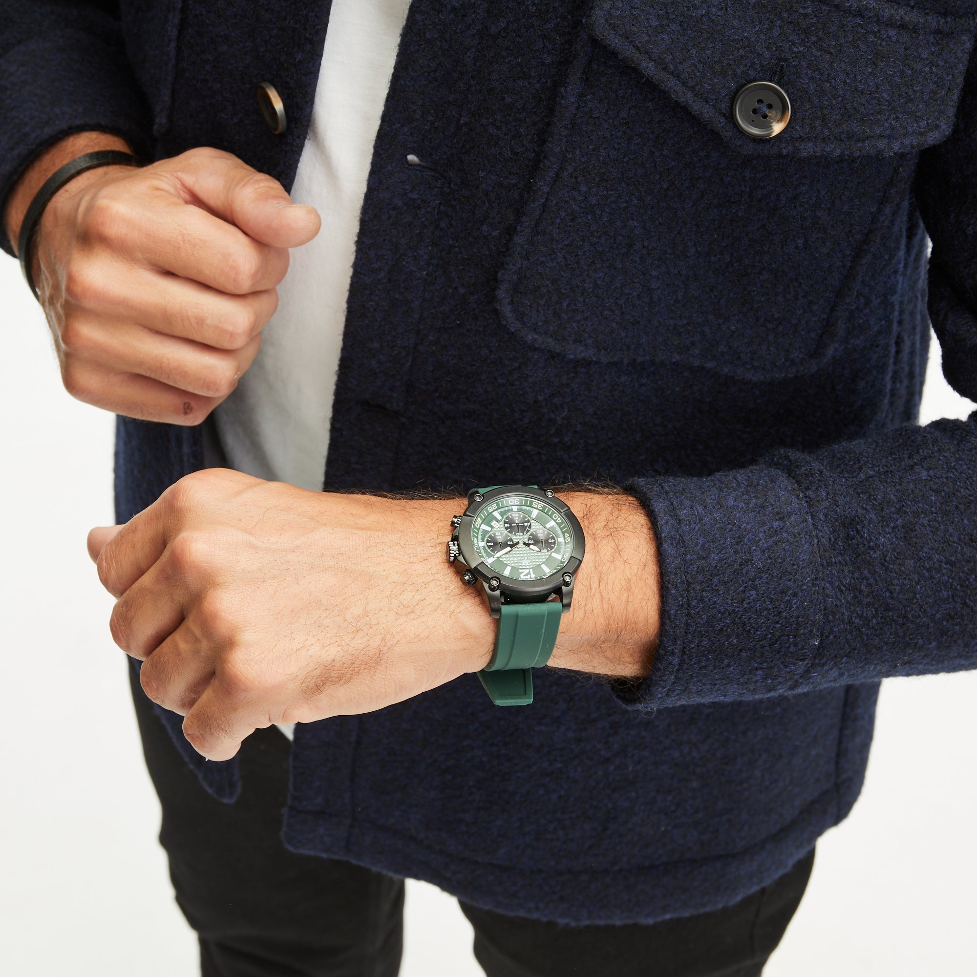 Eine Person in einem marineblauen Mantel trägt eine Fynch-Hatton-Armbanduhr - The Green Chrono an ihrem linken Handgelenk vor einem weißen Hintergrund.