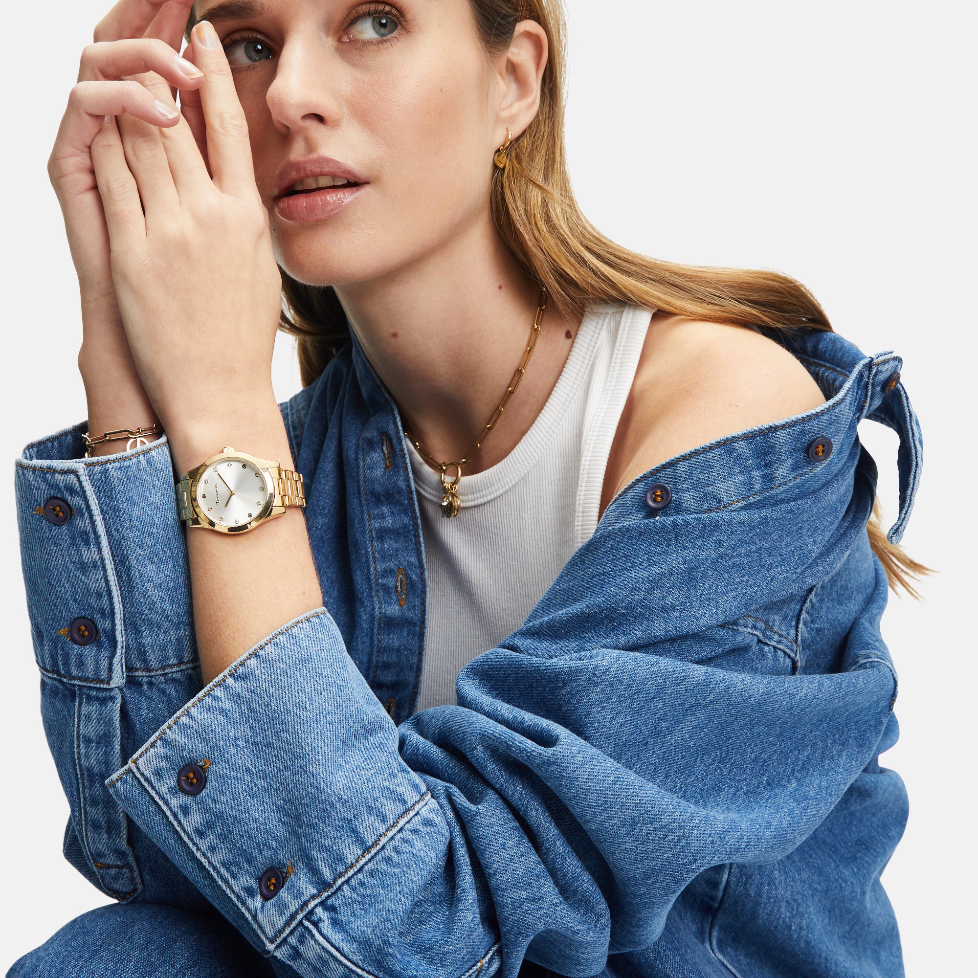 Frau in Jeansjacke und weißem Tanktop mit goldener Uhr und der Tamaris Halskette - Time to Smile von Tamaris, mit Blick zur Seite.