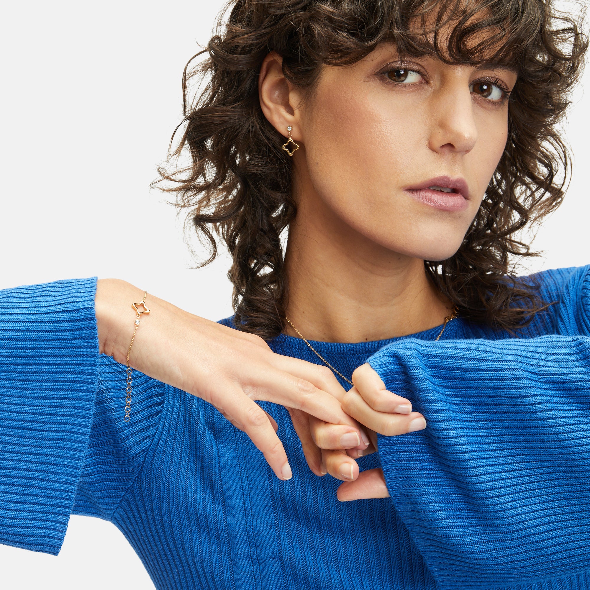 Tragebild von Apple of Eden: Frau in blauem Strickpullover mit zartem Schmuck – Ohrringe, Armband und Kette im modernen, femininen Look.