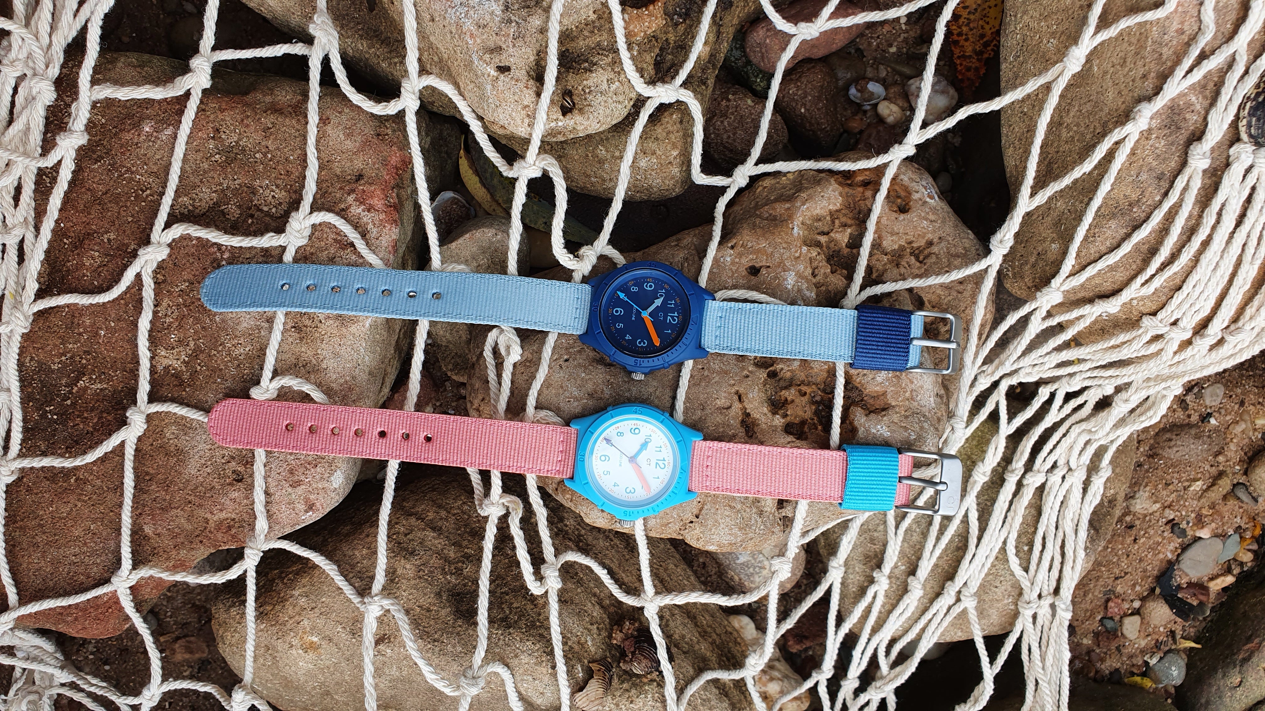 Zwei bunte Eco-Uhren von Cool Time Kids auf einem Fischernetz vor Steinen – nachhaltig, farbenfroh und ideal für kleine Umweltfreunde.