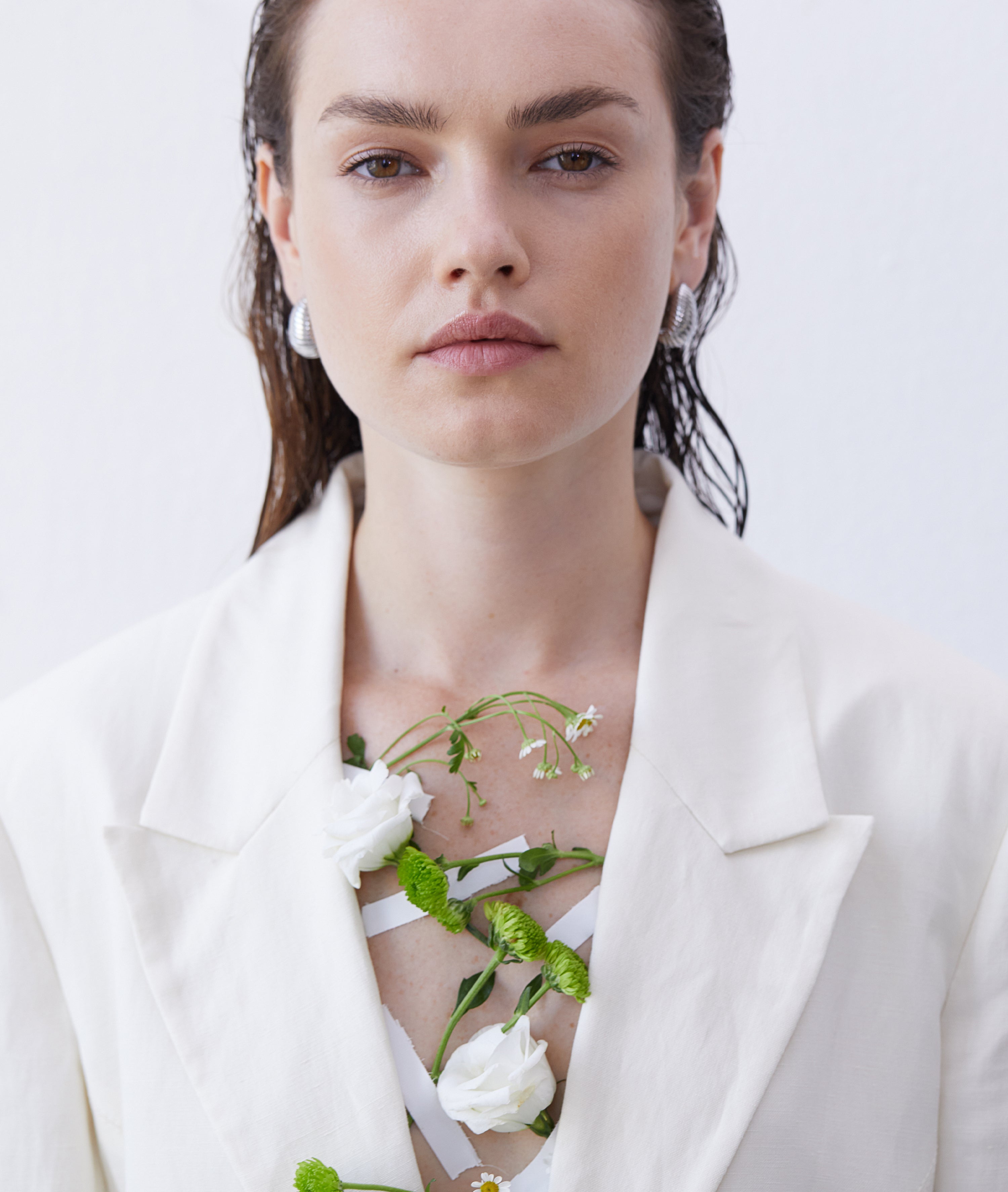 Frau in weißem Blazer mit silbernen Ohrringen, floral inszeniert mit weißen Blüten – modern, minimalistisch und natürlich.