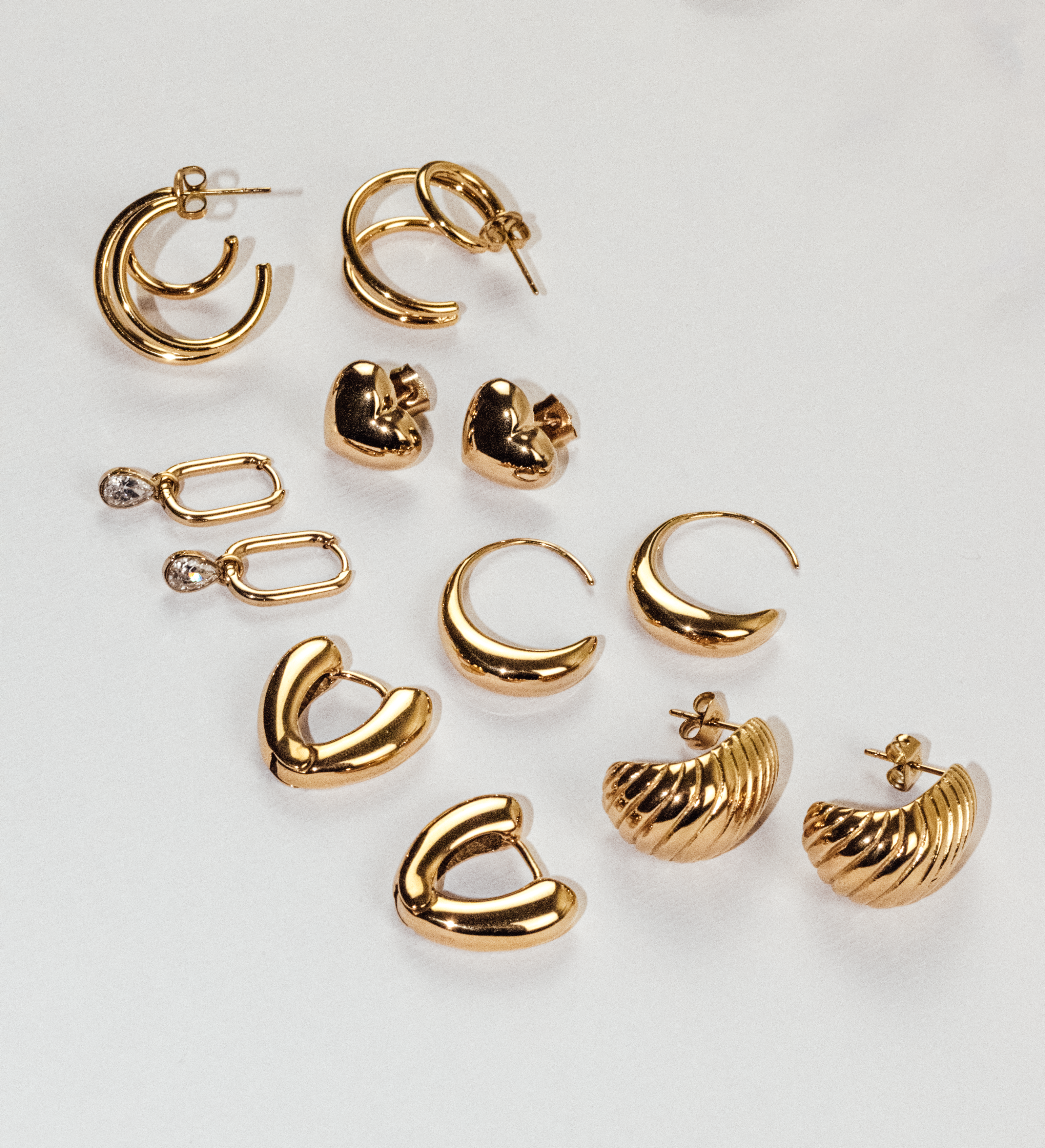 Goldene Echtzeit-Ohrringe in verschiedenen Designs – von schlicht bis auffällig – elegant arrangiert auf hellem Untergrund.