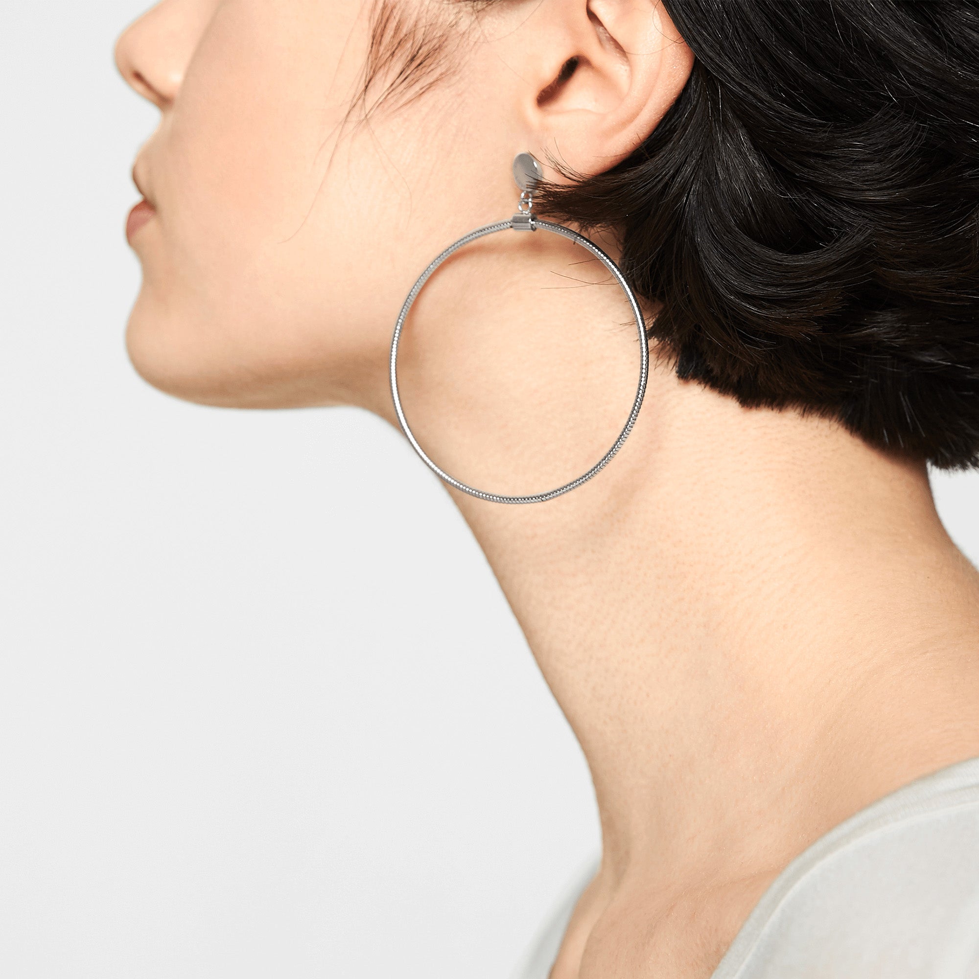 Eine Person mit kurzen dunklen Haaren trägt einen großen silbernen Ohrring, "The Retro One" aus der Liebeskind Berlin Creole Kollektion, an ihrem linken Ohr.