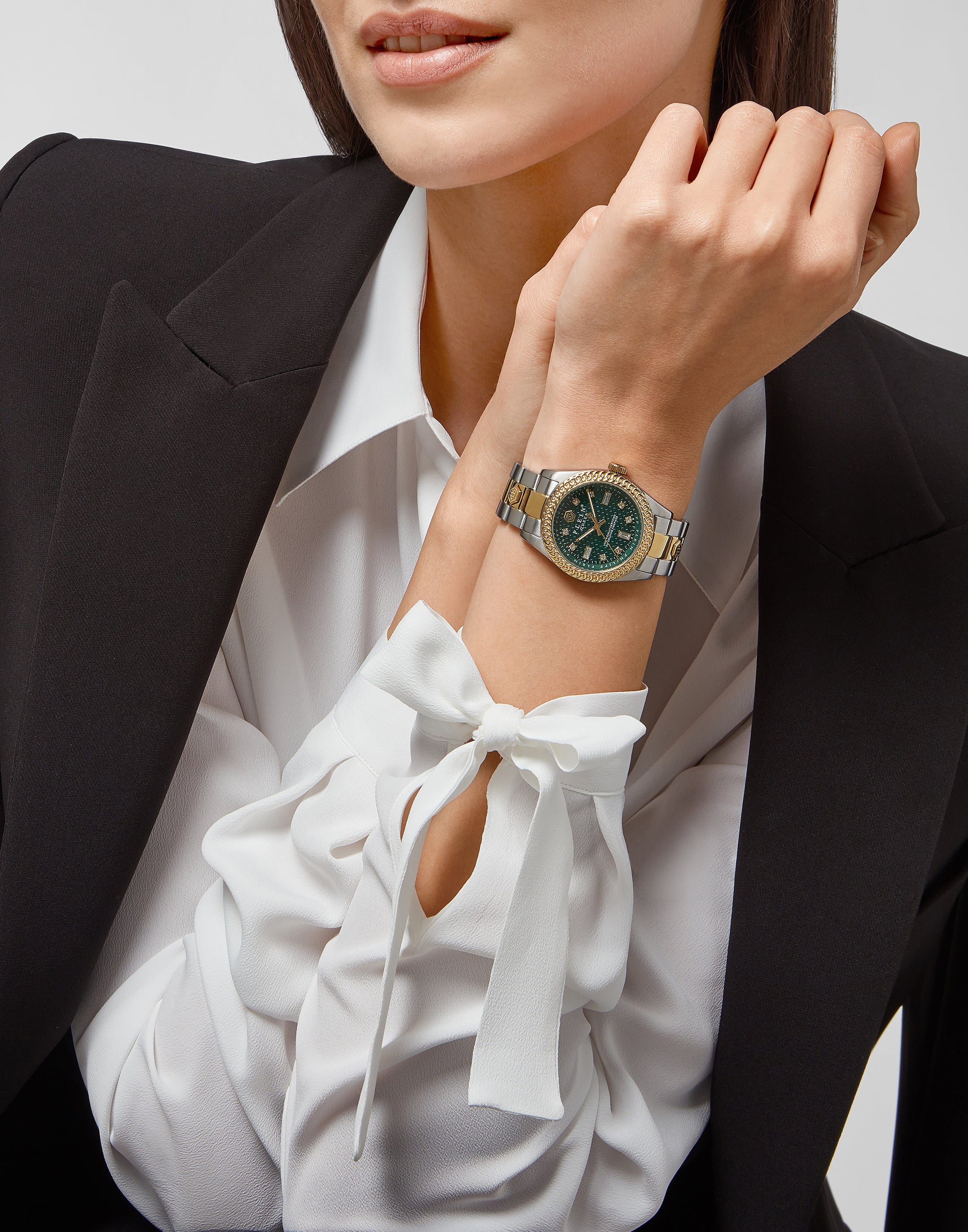 Image von PHILIPP PLEIN: Frau im eleganten Business-Look trägt auffällige Armbanduhr mit gold-silbernem Band und grünem Zifferblatt als Statement-Piece.