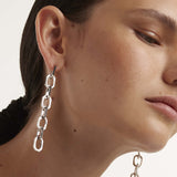 Eine Frau trägt den PDPaola Ohrhänger - The Chain an ihrem linken Ohr und betont damit den eleganten Silberschmuck von PDPaola, der durch ein natürliches Make-up und eine glatte Haut ergänzt wird.