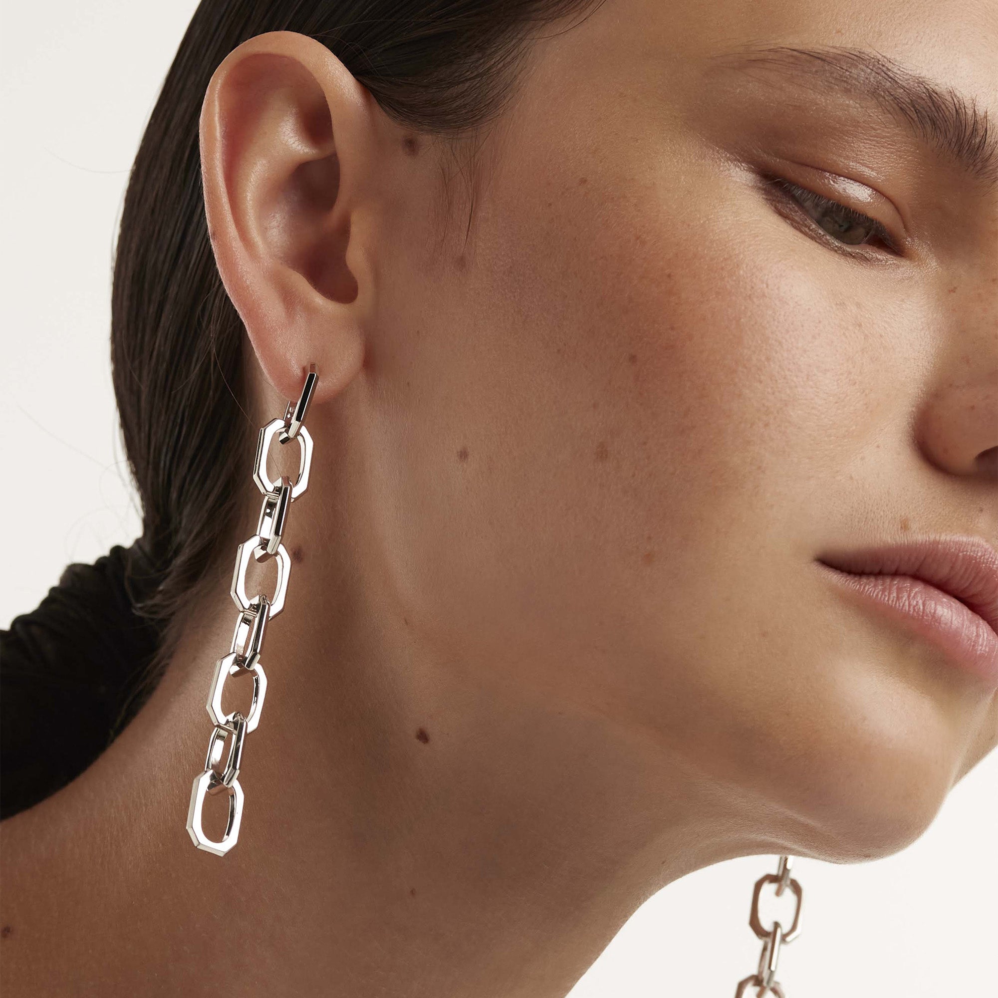Eine Frau trägt den PDPaola Ohrhänger - The Chain an ihrem linken Ohr und betont damit den eleganten Silberschmuck von PDPaola, der durch ein natürliches Make-up und eine glatte Haut ergänzt wird.