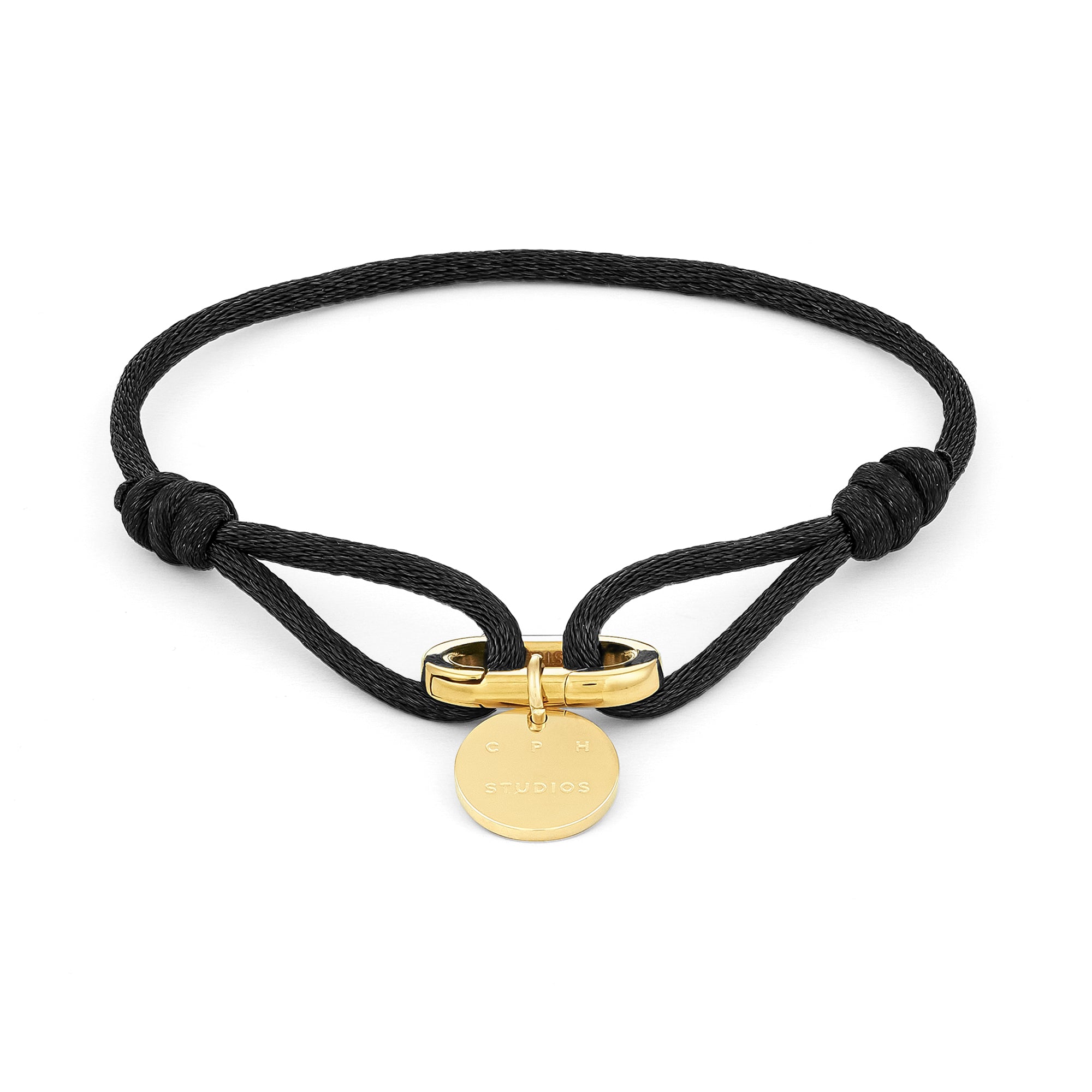 Armband - Fabric Link von Copenhagen Studios: schwarzes Gliederarmband aus Stoff mit goldenem Verschluss und rundem, goldenem Anhänger mit eingraviertem Text, inspiriert vom charakteristischen Stil der Marke.