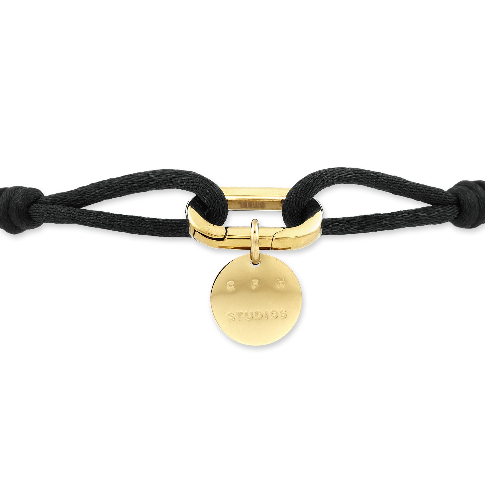 Das COPENHAGEN STUDIOS Armband - Fabric Link von Copenhagen Studios besteht aus schwarzem Stoff mit einem goldenen Verschluss und einem runden goldenen Anhänger, in den der Markenname eingraviert ist.