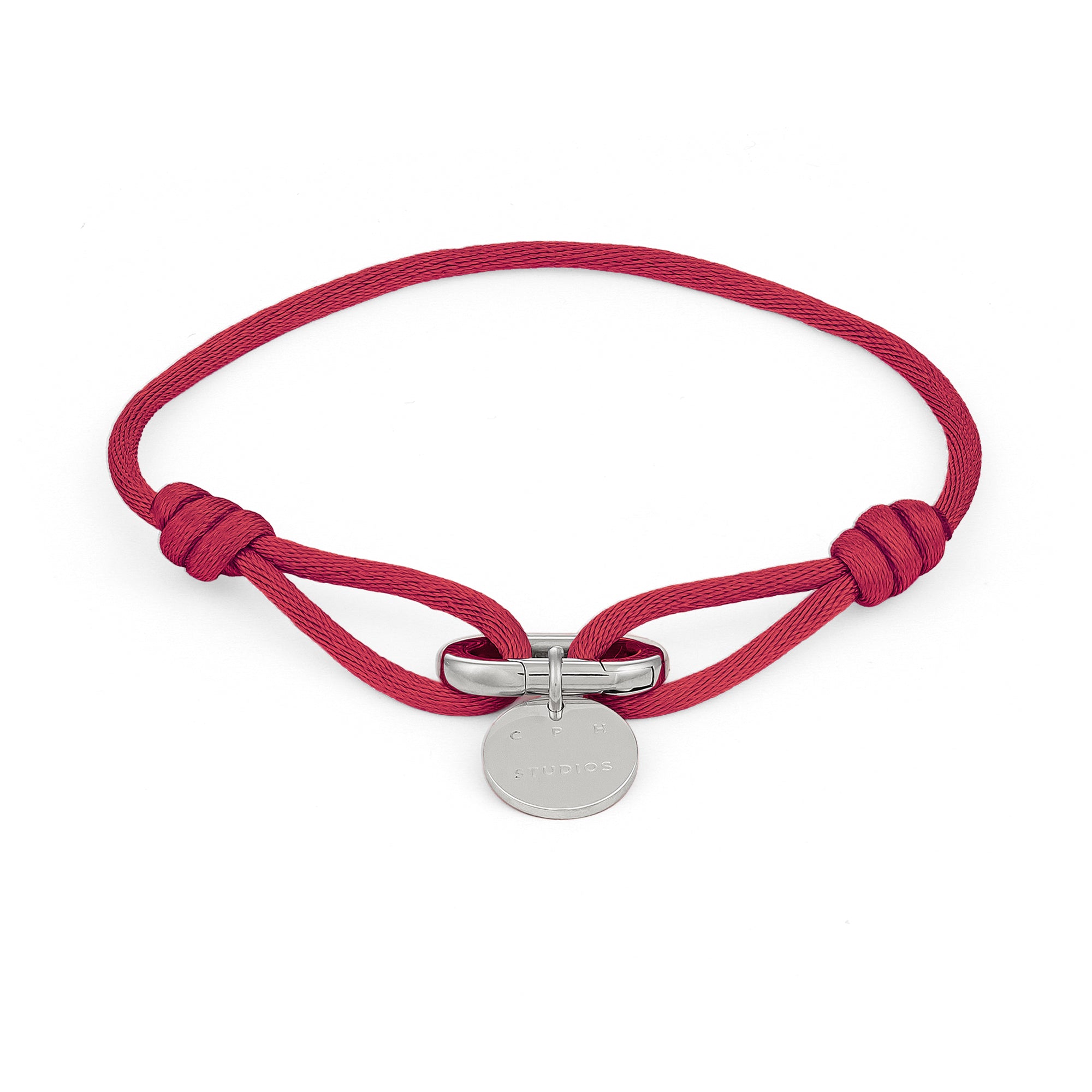 Das COPENHAGEN STUDIOS Armband - Fabric Link von Copenhagen Studios besteht aus einem roten Stoffband mit einem runden silbernen Anhänger und einer Metallschließe - ein stilvolles, elegantes Accessoire.