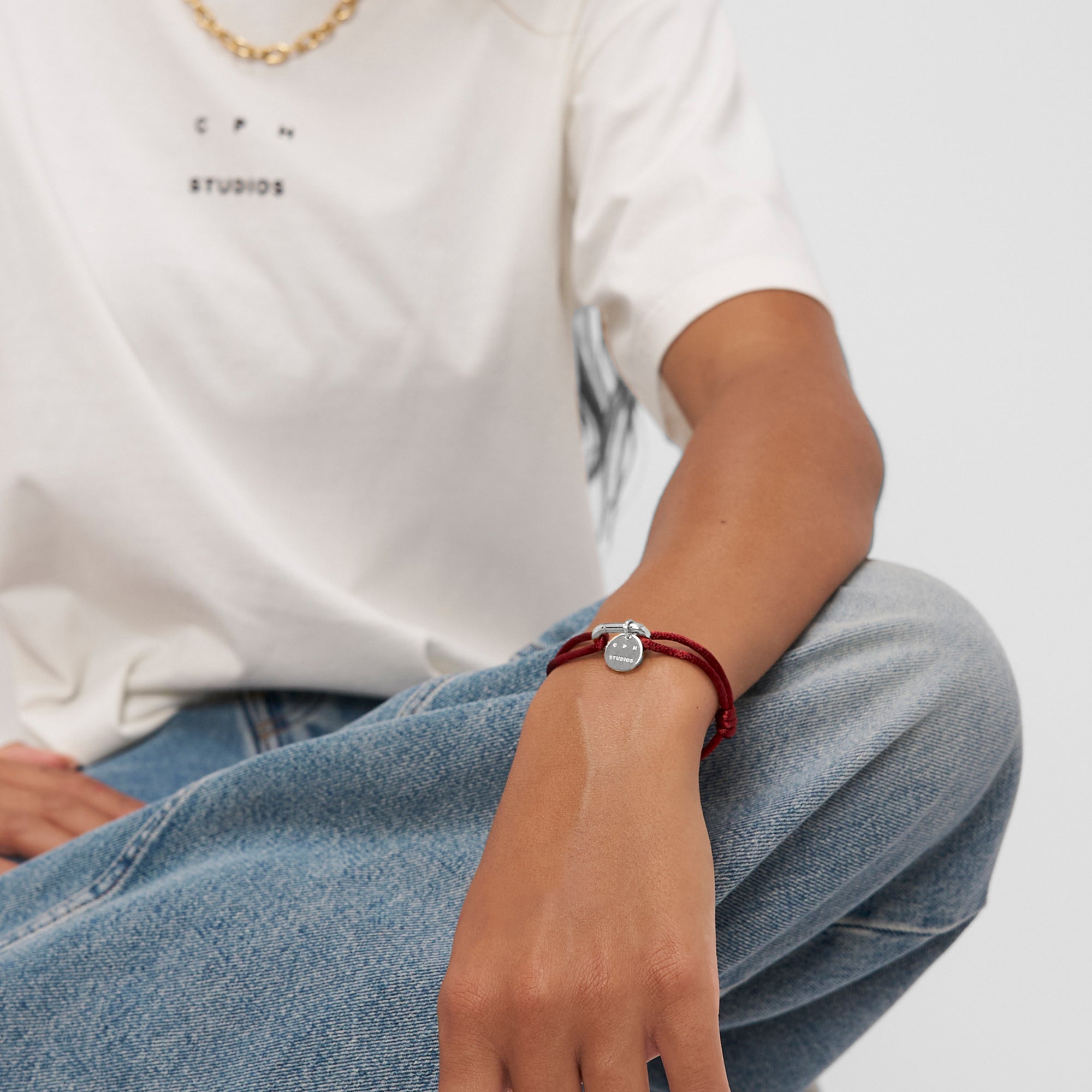 Person in blauer Jeans und weißem T-Shirt trägt im Schneidersitz ein Copenhagen Studios Armband - Fabric Link mit einem runden Anhänger.