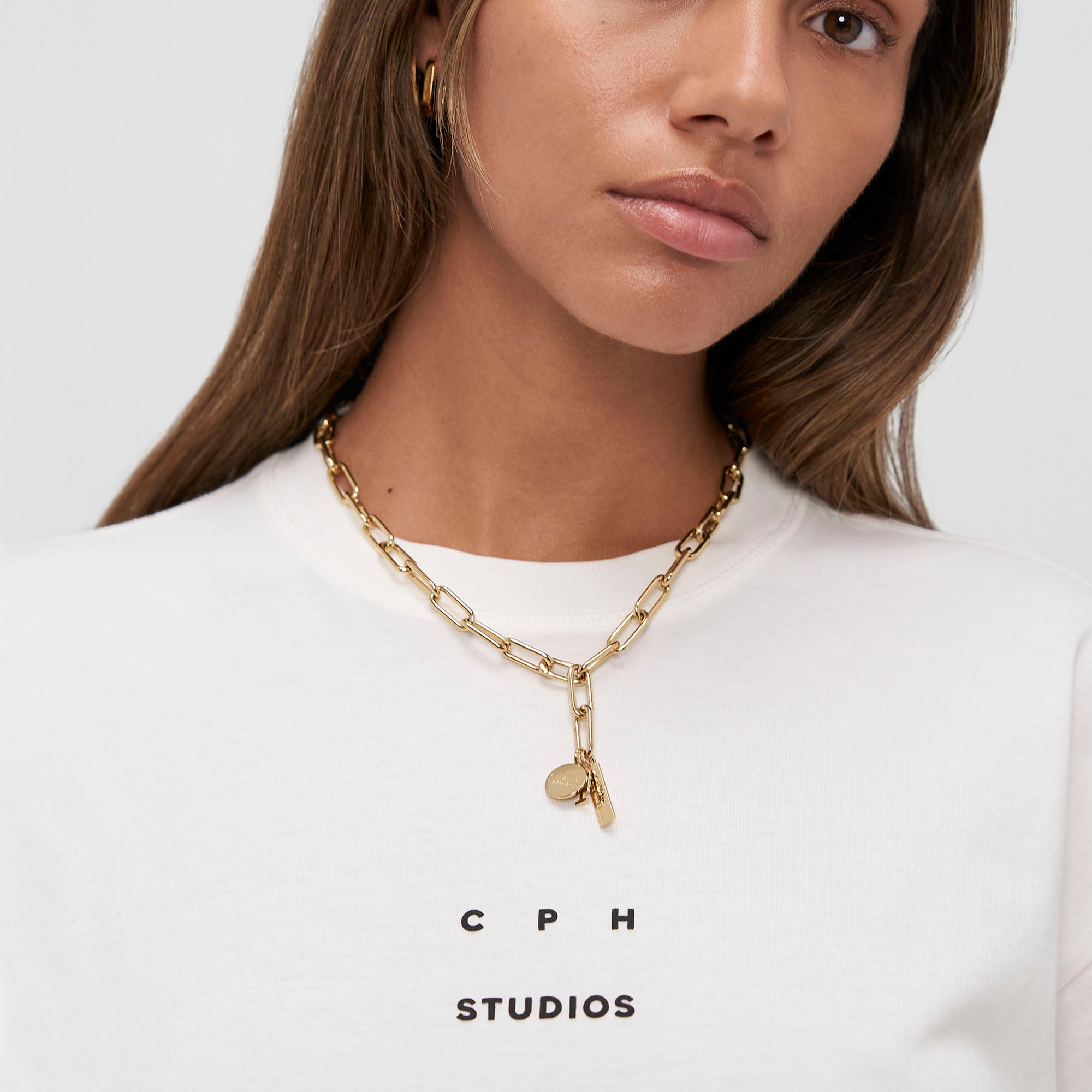 Frau trägt die COPENHAGEN STUDIOS Halskette - Bold Set und ein weißes Hemd von Copenhagen Studios, von den Schultern aufwärts gezeigt.