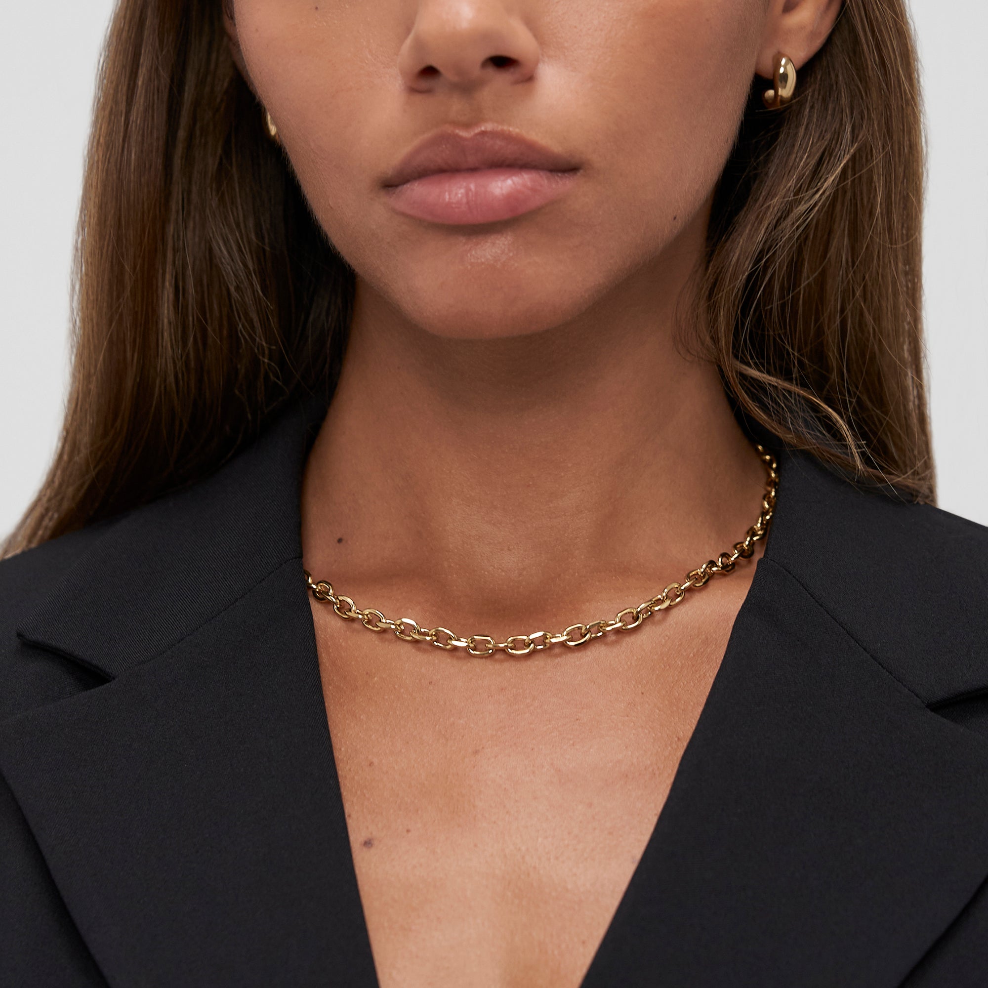 Frau trägt die Halskette Copenhagen Studios - Basic Chains, goldene Ohrringe und einen schwarzen Blazer, von den Schultern aufwärts fotografiert.