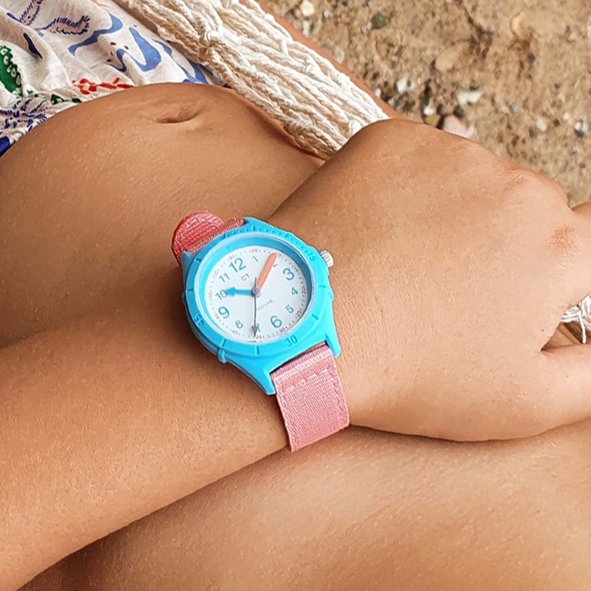 Eine Person trägt die Cool Time Kids Armbanduhr - The Cool Sustainable von Cool Time, eine blau-rosa Uhr aus recyceltem Ozeanplastik, während sie an einem Sandstrand liegt.