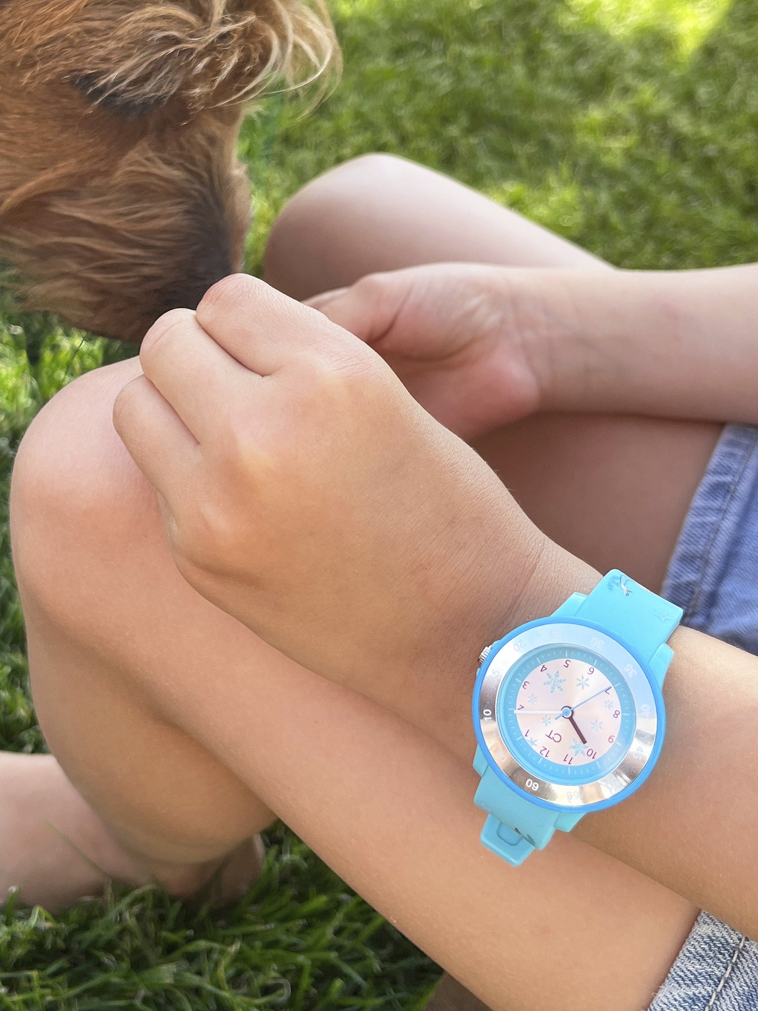Ein Kind, das eine Cool Time Kids Armbanduhr - The Cool Ice Princess von Cool Time trägt, sitzt im Gras und streichelt einen braunen Hund mit angezogenen Knien.