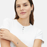 Selbstbewusst posierende Frau in weißem T-Shirt mit mehrlagigem Schmuck, darunter die Tamaris Halskette - The Sparkling Stars, sowie ein Armband und kleine Ohrringe.