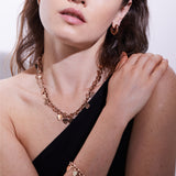 Eine Frau trägt die Echtzeit Creole - The Modern Basic von Echtzeit: ein goldenes Schmuckset mit Herz-Halskette, Armband und Statement-Ring-Ohrringen - ein modernes, elegantes Accessoire für Frauen, das perfekt zu ihrem schwarzen Outfit passt.