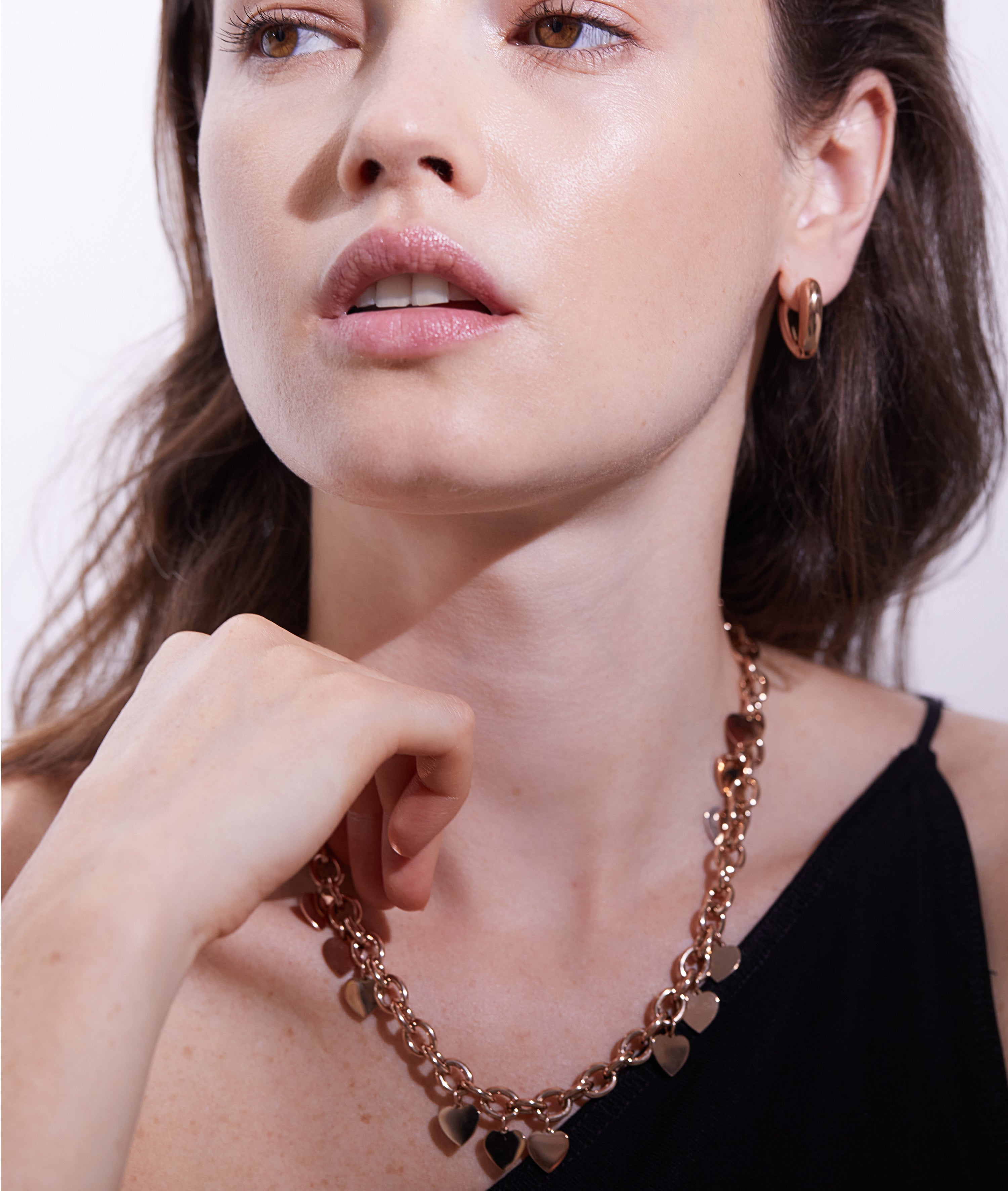 Eine Frau trägt die Echtzeit Creole - The Modern Basic Ohrringe und eine goldene Herzkette mit einem schwarzen ärmellosen Oberteil und schaut zur Seite - stilvolles Echtzeit-Accessoire mit modernem Design für Frauen.