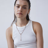 Frau mit nassen Haaren in einem weißen Tank-Top und mehrlagigen Halsketten, mit der Echtzeit Creole - Like Diamonds von Echtzeit, vor einem schlichten hellen Hintergrund.