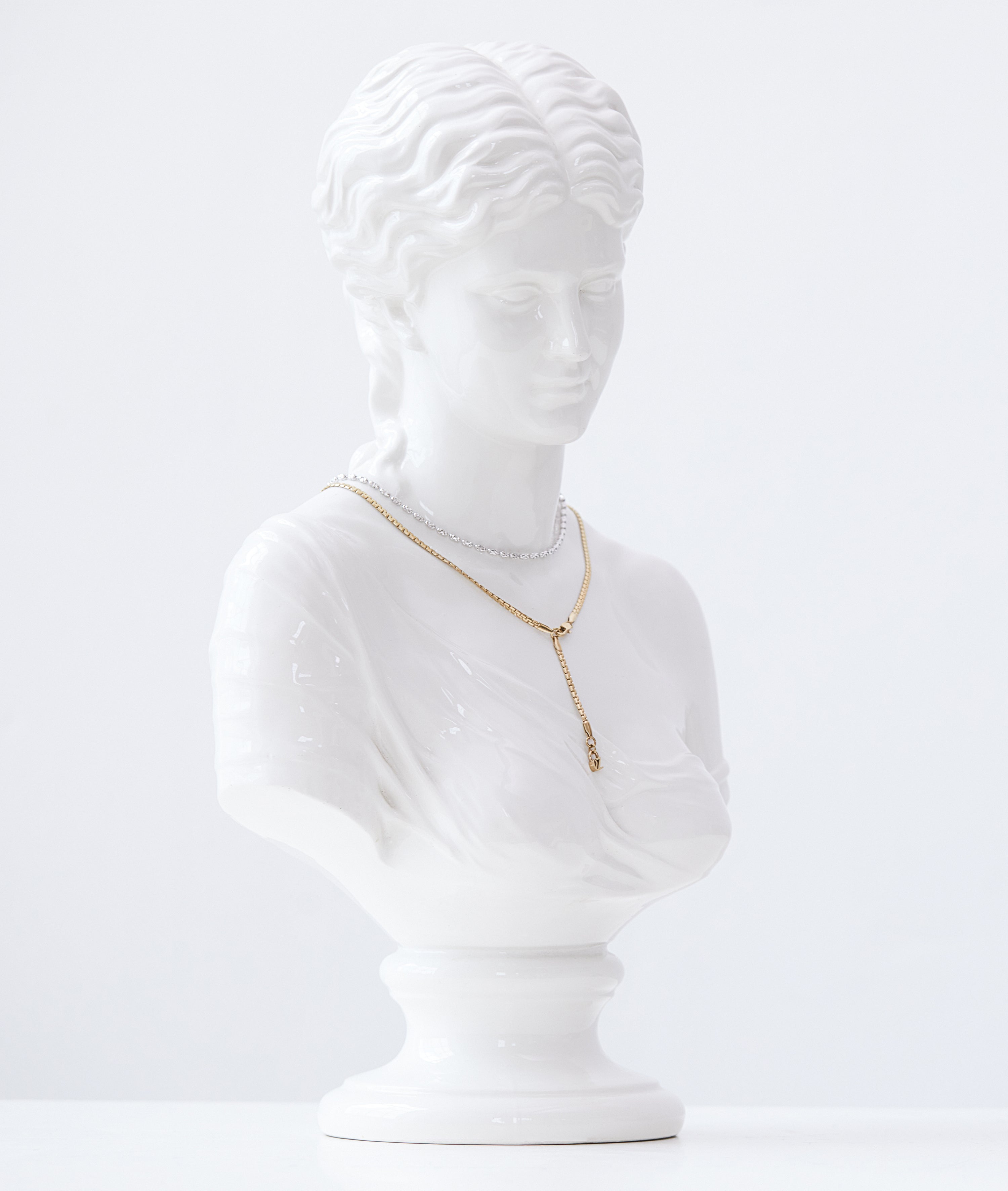 Weiße Marmorbüste einer Frau präsentiert die Echtzeit Halskette - The Sleek One von Echtzeit, eine goldene Halskette, die sich ideal für den trendigen Layering-Look eignet, vor einem schlichten weißen Hintergrund.