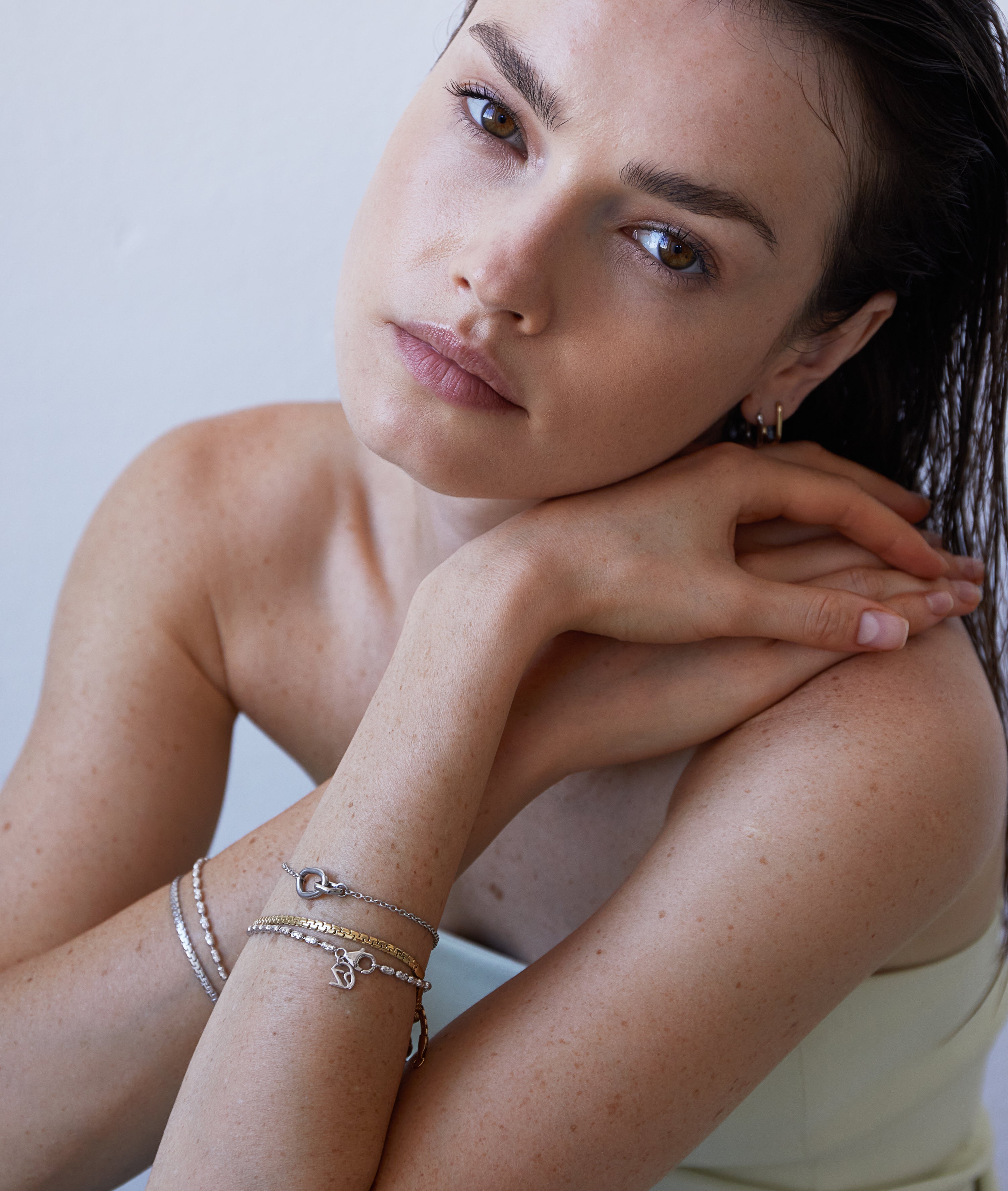 Frau mit nackten Schultern stützt ihr Kinn auf die Hände, trägt das Echtzeit Armband - Like Diamonds von Echtzeit und schaut in die Kamera.