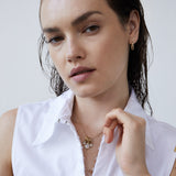 Eine Frau mit nassen Haaren in einem weißen ärmellosen Shirt trägt die Echtzeit Creole - Like Diamonds Goldohrringe von Echtzeit und geschichtete Goldketten, darunter einen zarten Tropfenanhänger.